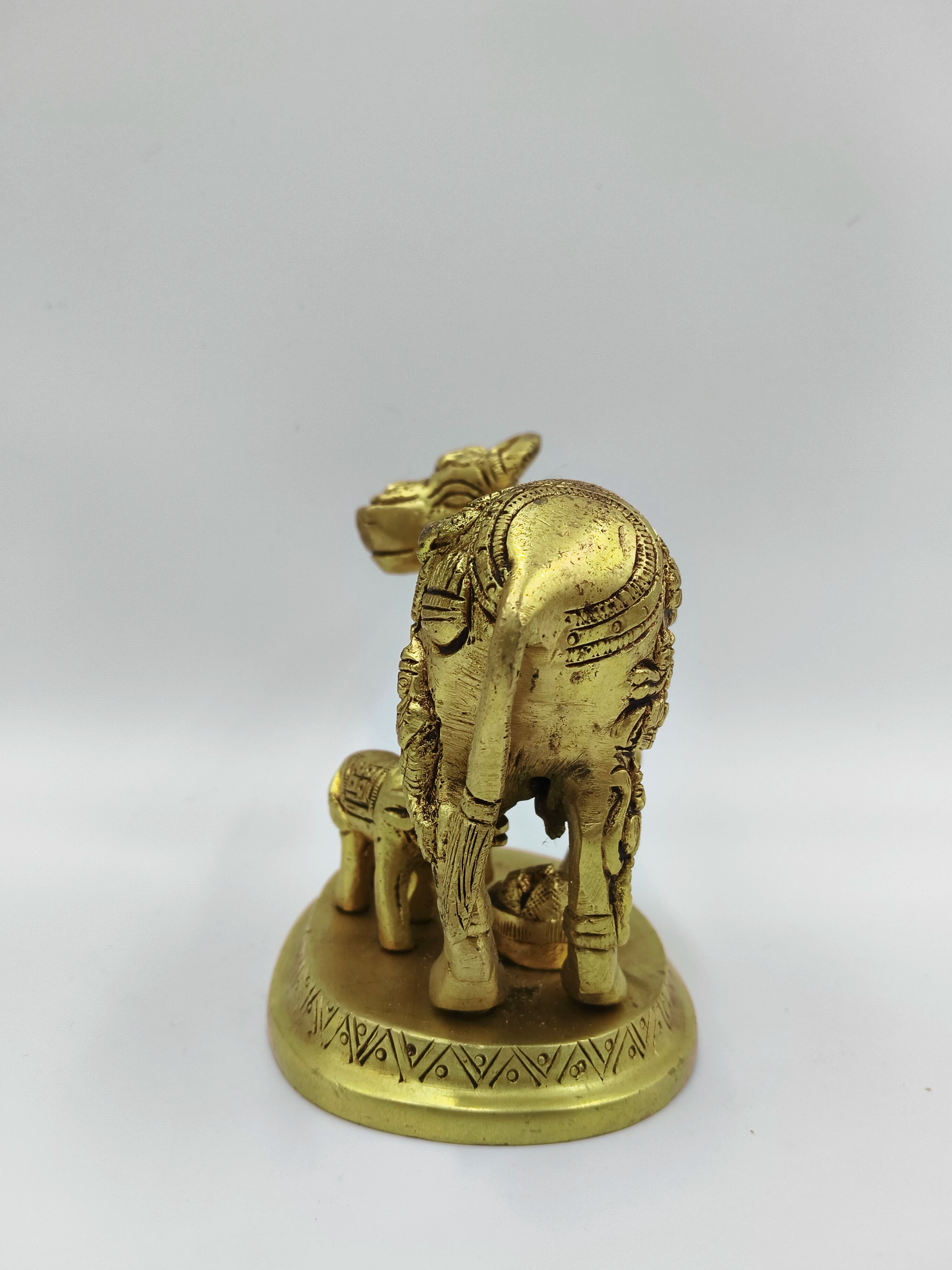 Rear view of small brass cow and calf sculpture with divine figure on base