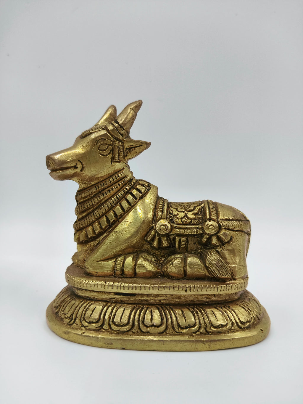 Small brass Nandi bull figurine sitting on decorative base, side view
