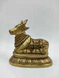 Small brass Nandi bull figurine sitting on decorative base, side view