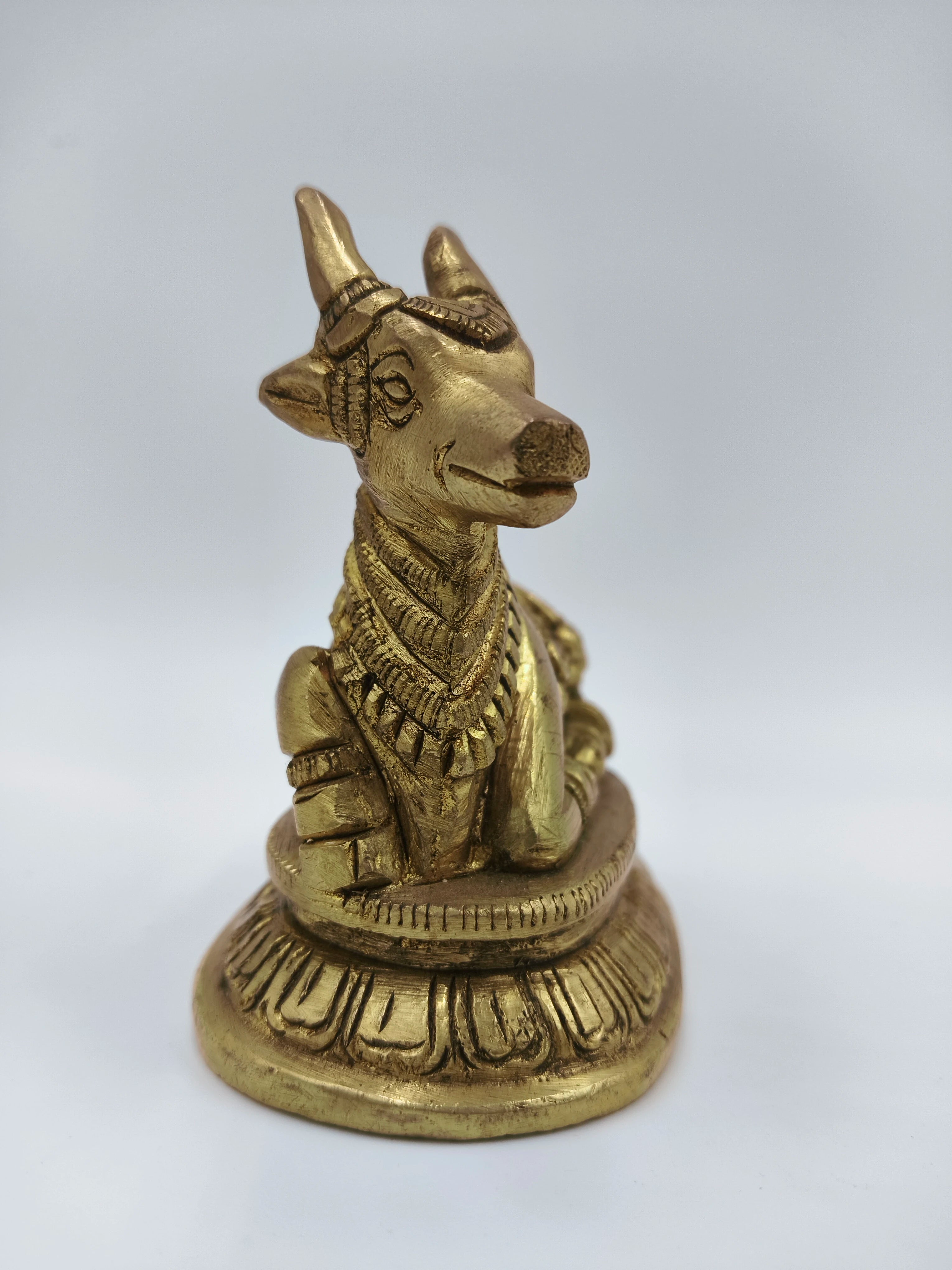 Small brass Nandi figurine sitting on decorative base, side view