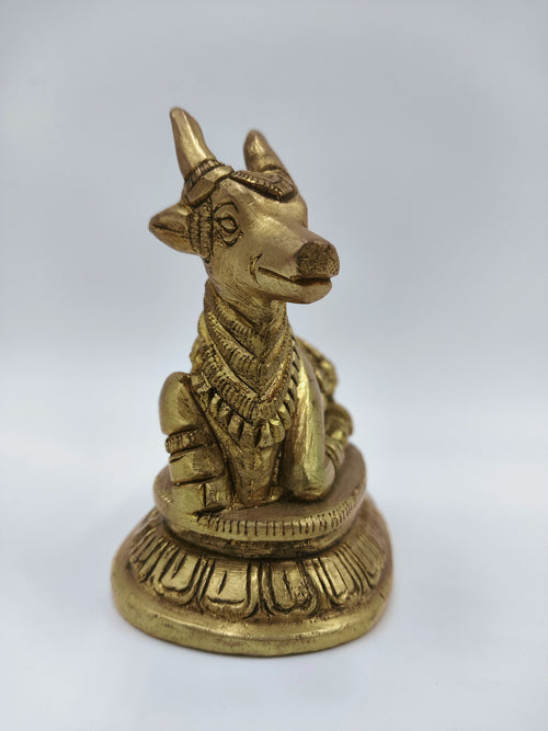 Small brass Nandi figurine sitting on decorative base, side view