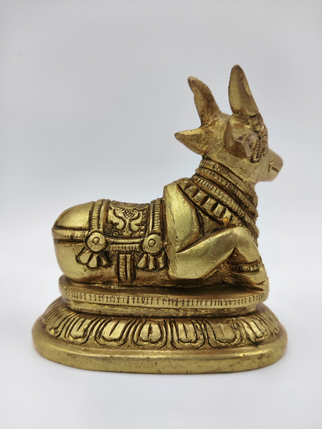 Side view of small brass Nandi bull figurine seated on a decorative base