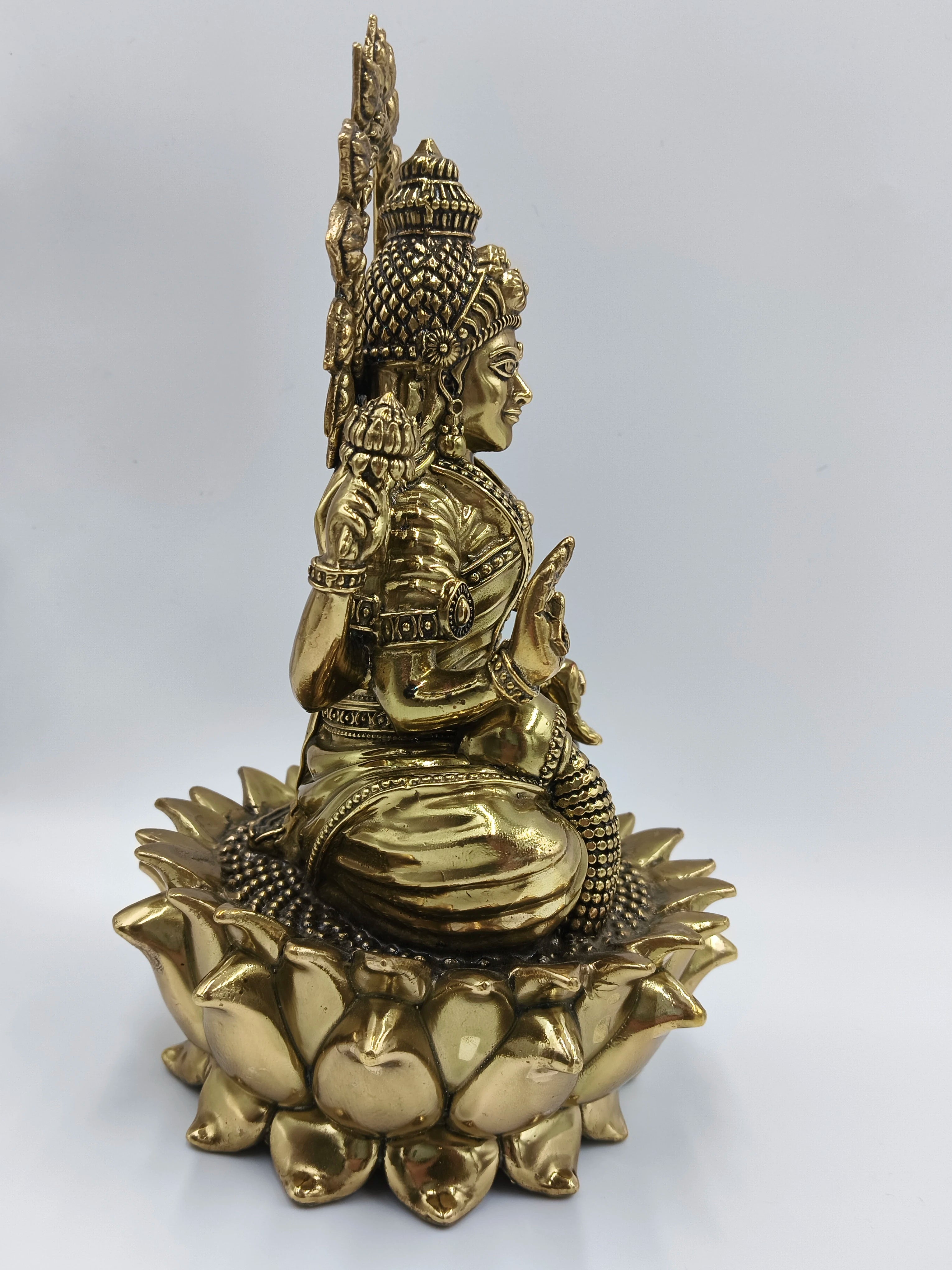 Side view of a large brass statue of Goddess Lakshmi sitting on a lotus