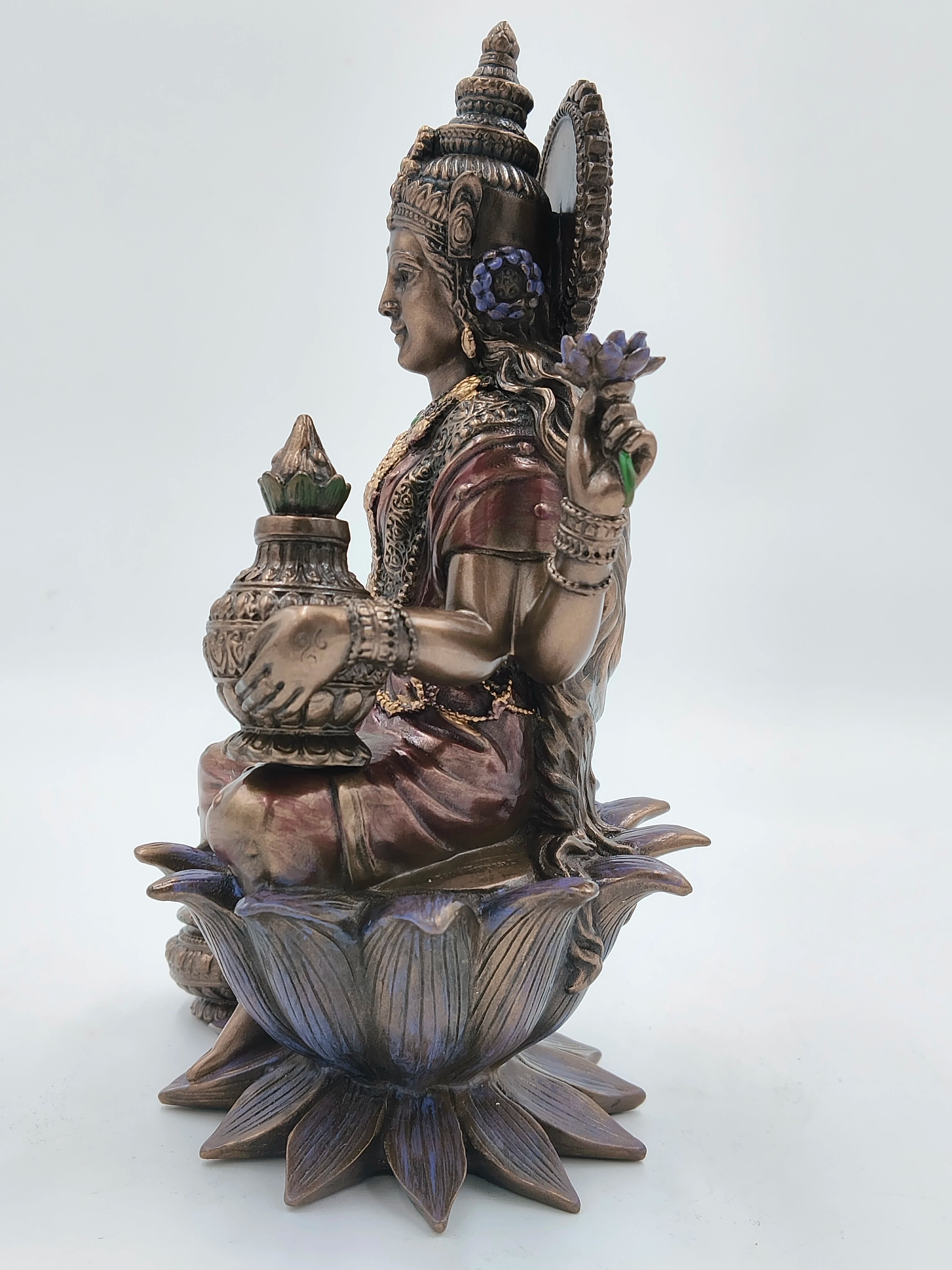 Side view of polyresin Lakshmi statue seated on a lotus flower holding a lotus and pot