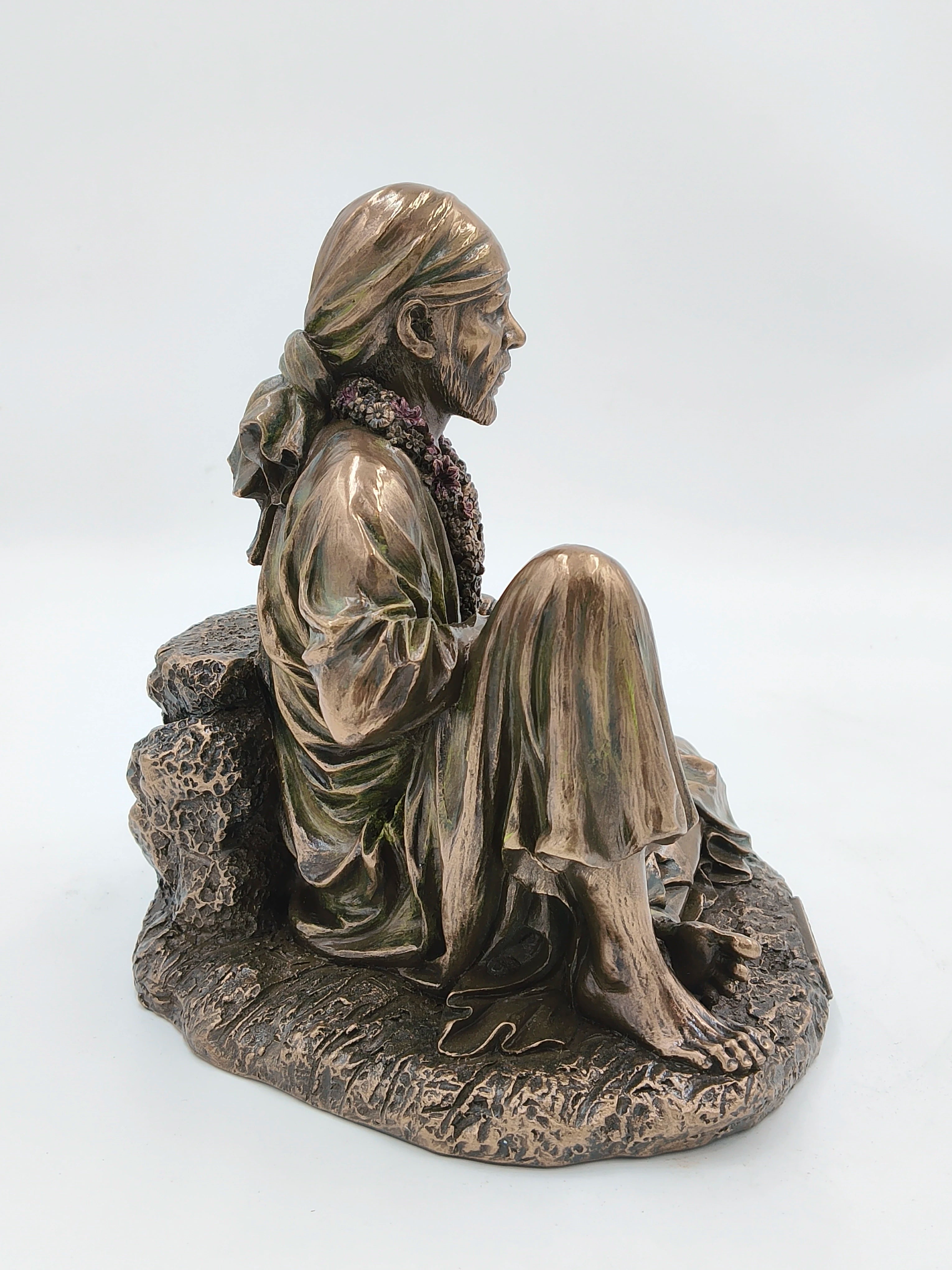 Side view of large polyresin Shirdi Baba statue seated with headscarf and floral garland
