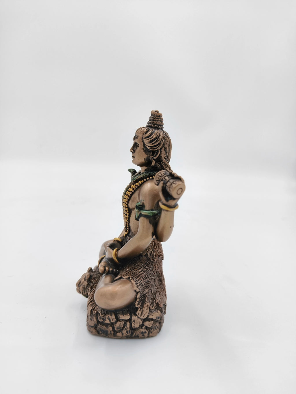 Side view of small polyresin statue depicting seated Shiva with detailed ornaments