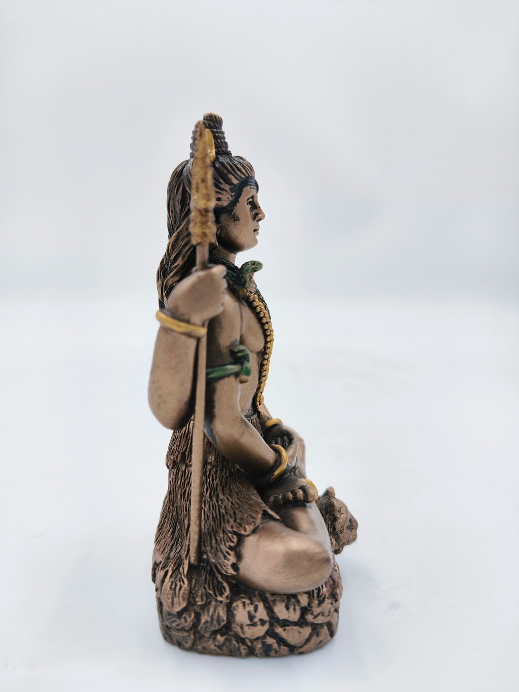 Side view of small polyresin Lord Shiva statue seated with trident and snake