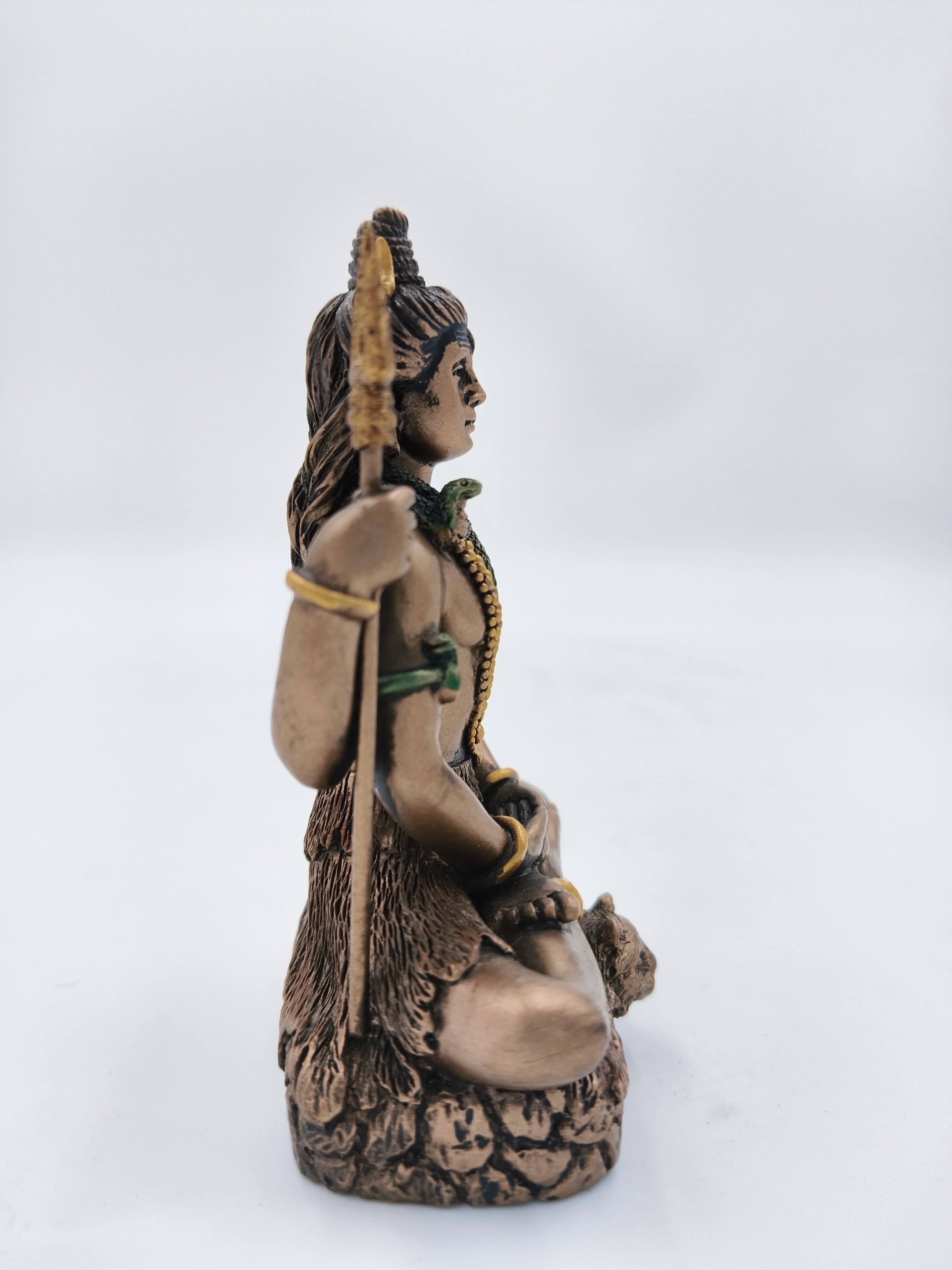 Side view of small polyresin Lord Shiva statue seated with trident and snake