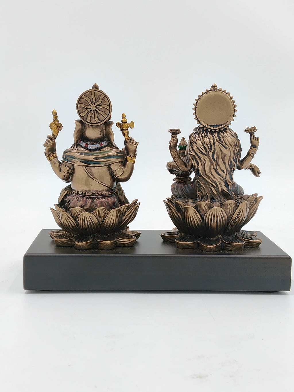 Back view of small polyresin Ganesh and Lakshmi statues seated on lotus base on black platform