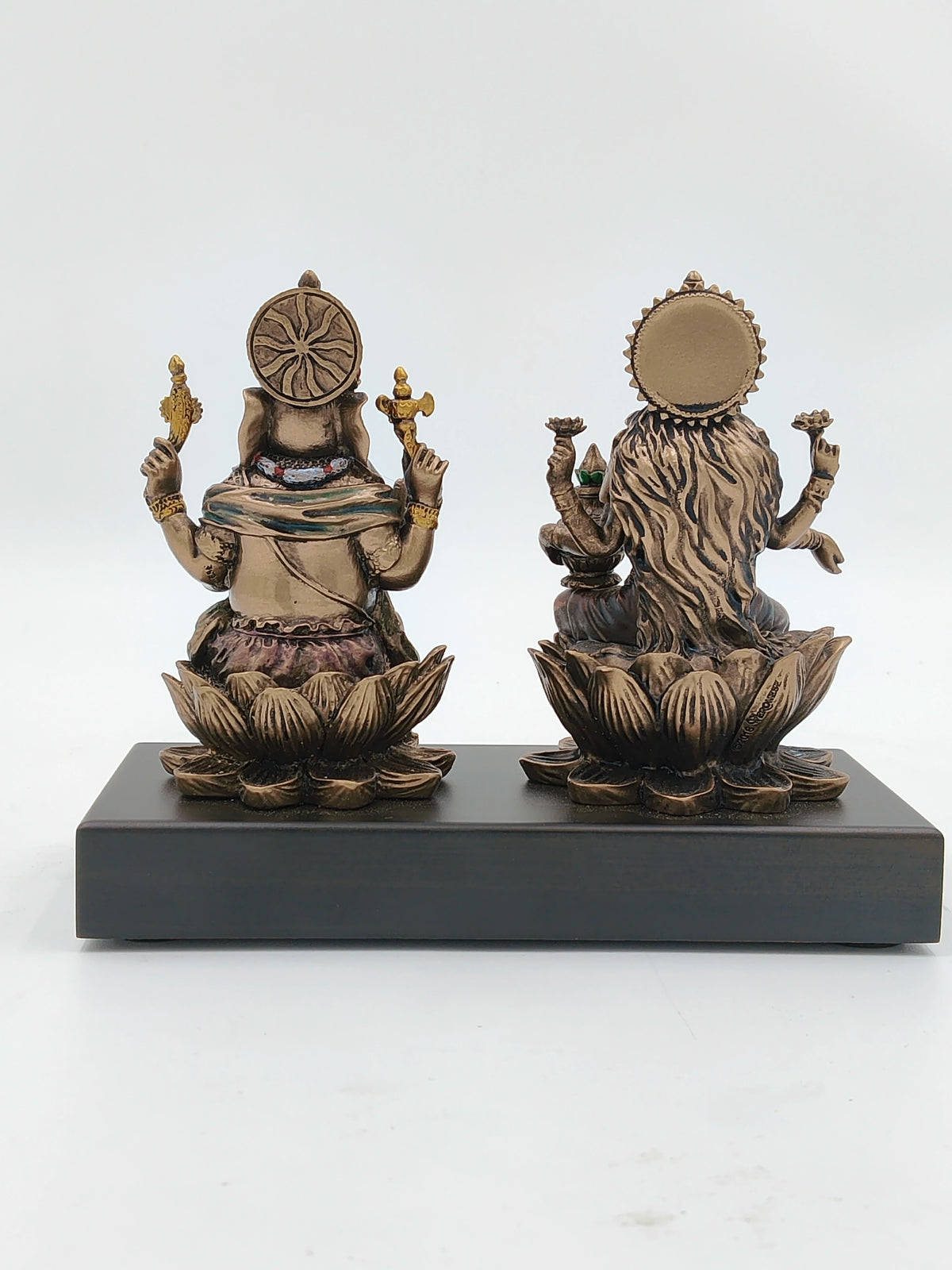Back view of small polyresin Ganesh and Lakshmi statues seated on lotus base on black platform