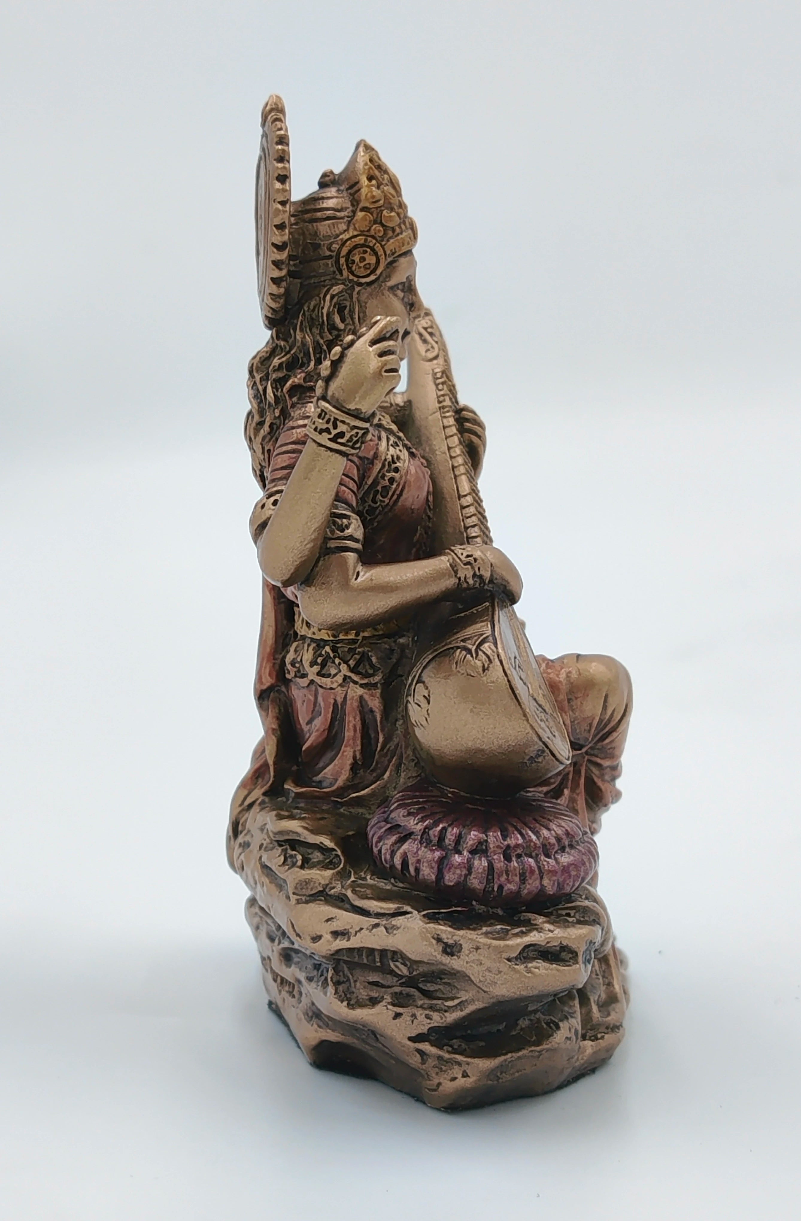 Side view of small polyresin Saraswathi statue playing veena on cushion