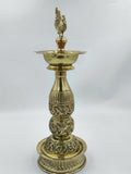 Large brass lamp with intricate floral engravings and peacock figurine on top