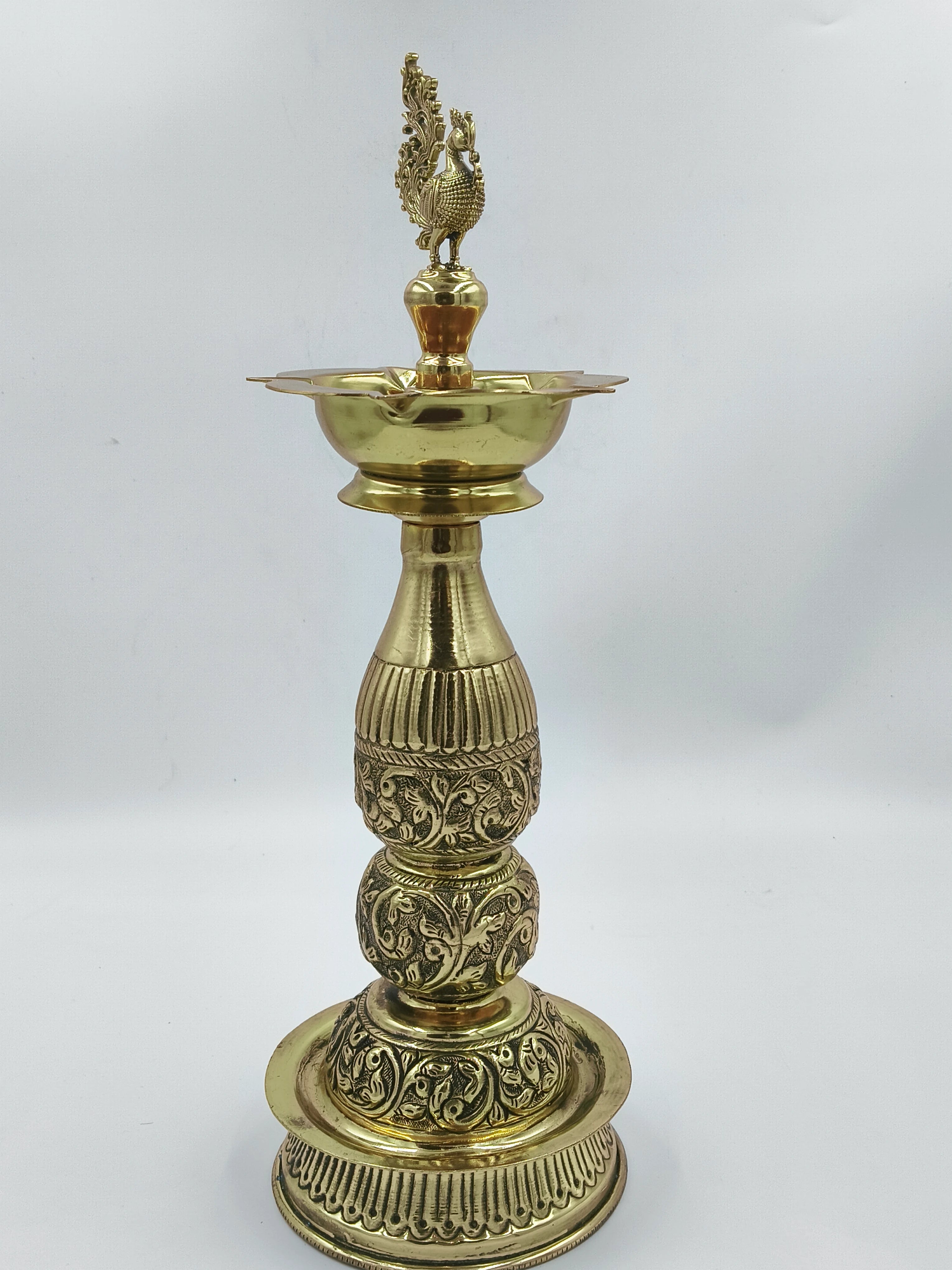 Large brass lamp with intricate floral engravings and peacock figurine on top
