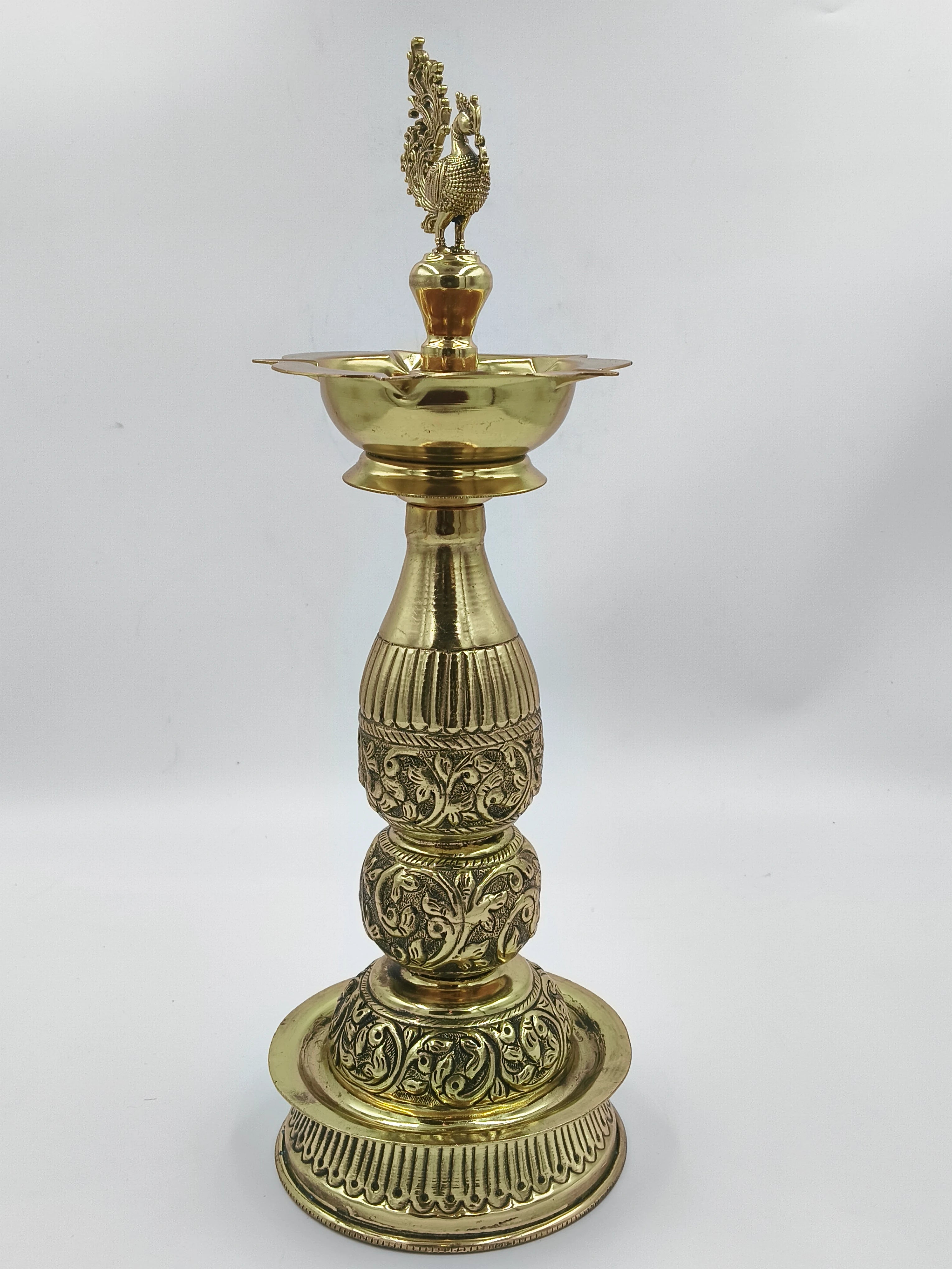 Tall brass lamp with intricate floral carvings and peacock finial