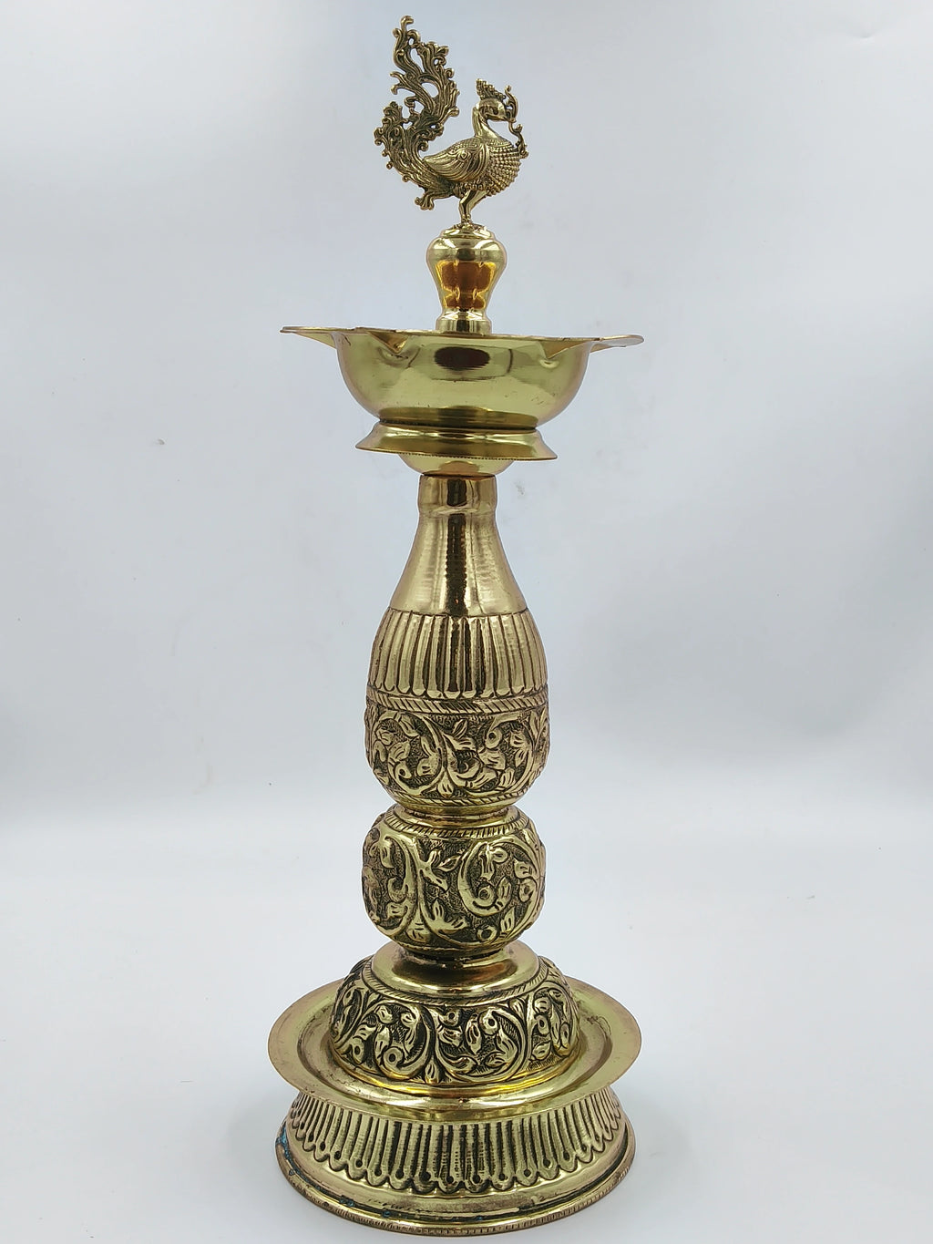 Tall traditional brass lamp with intricate engraved patterns and peacock finial
