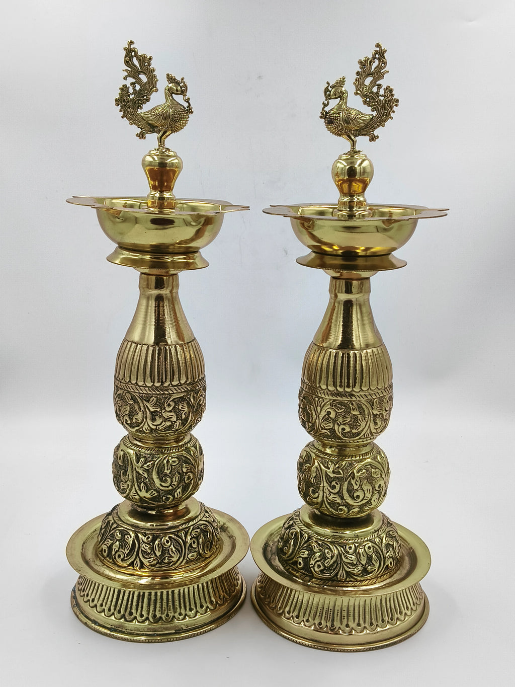 Pair of tall brass lamps with intricate engraved patterns and peacock design