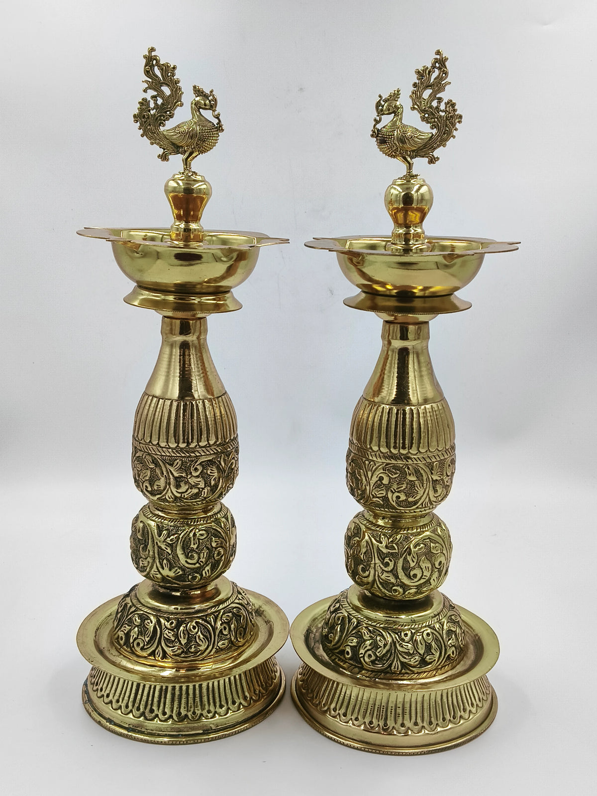 Pair of tall brass lamps with intricate engraved patterns and peacock design