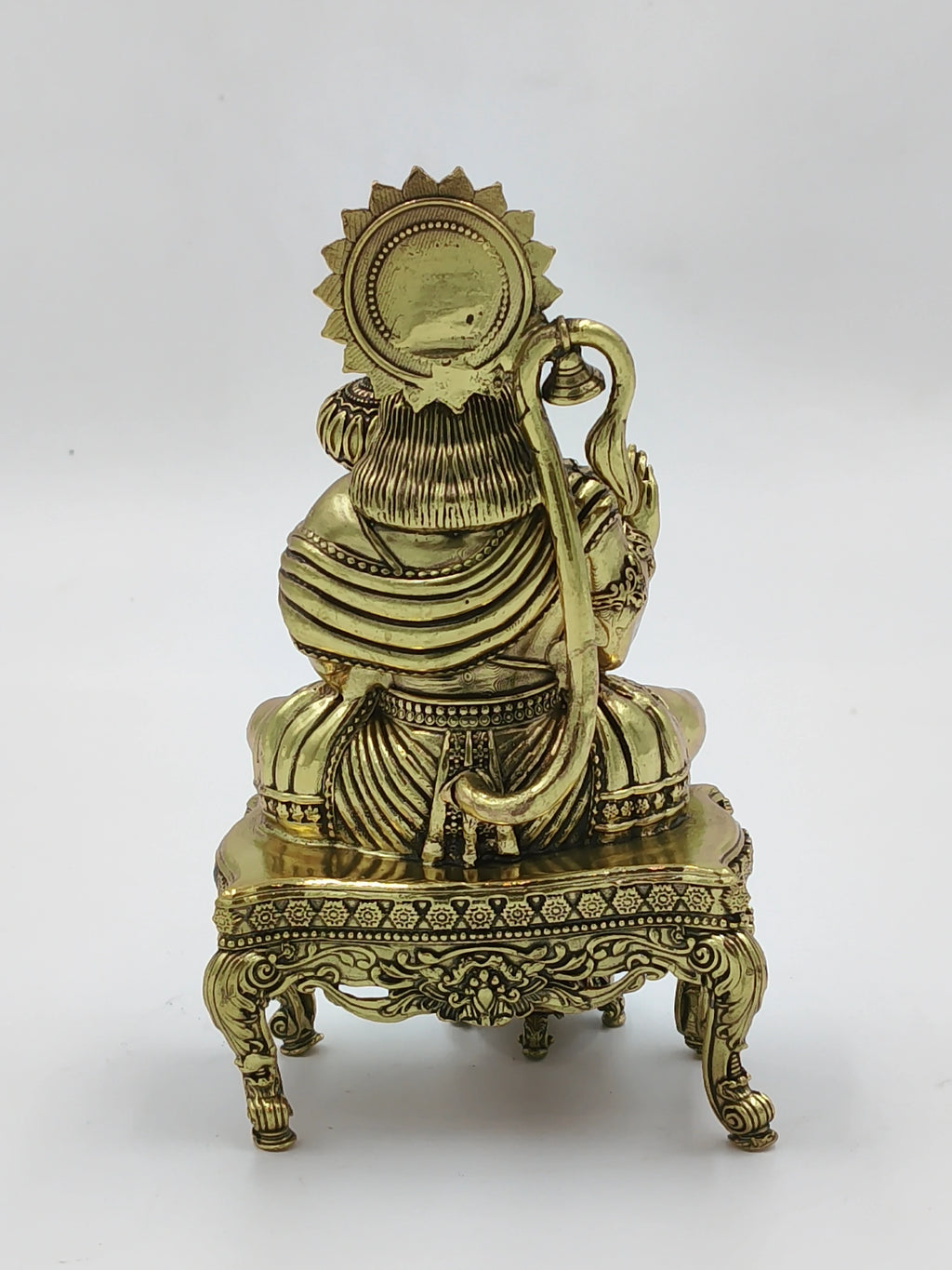 Back view of brass Hanuman figurine sitting on ornate chowki