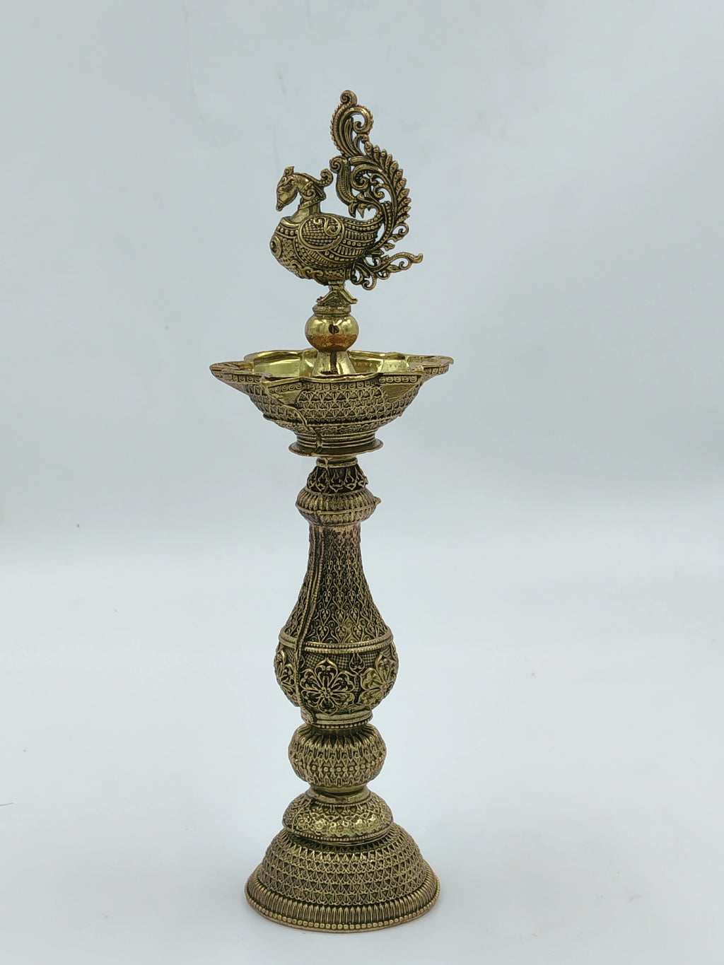 Tall brass lamp with intricate engravings and peacock design on top