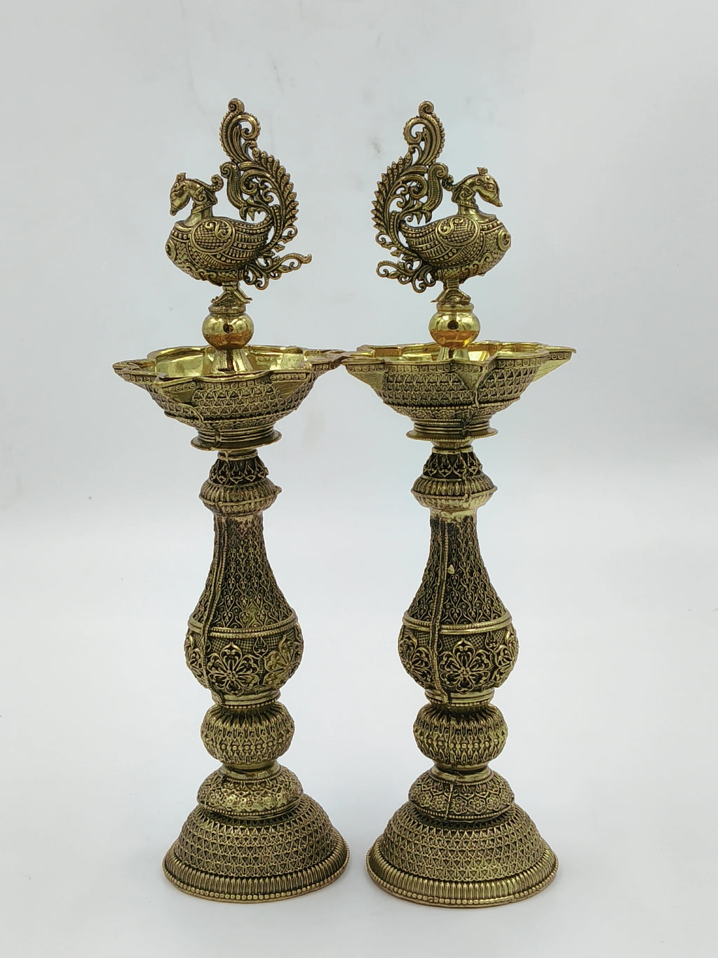 Pair of tall decorative brass lamps with intricate floral and peacock designs