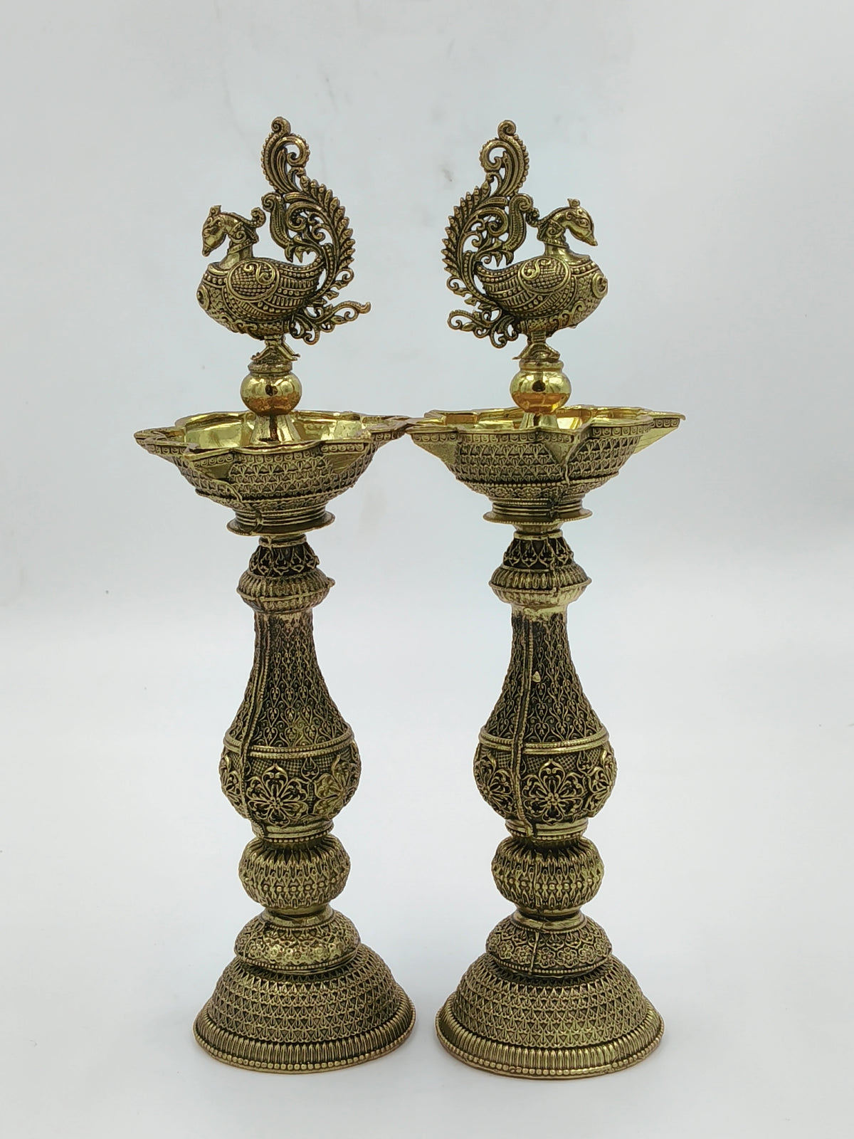 Pair of tall decorative brass lamps with intricate floral and peacock designs