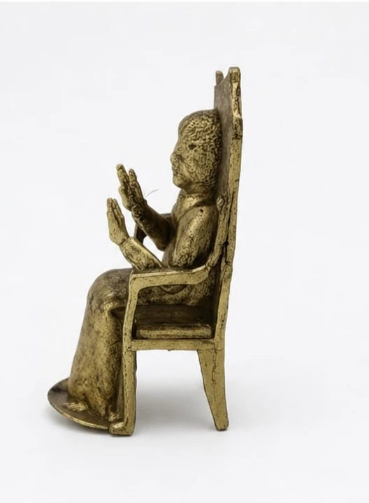 Side view of small brass Sai Baba figurine seated on a chair