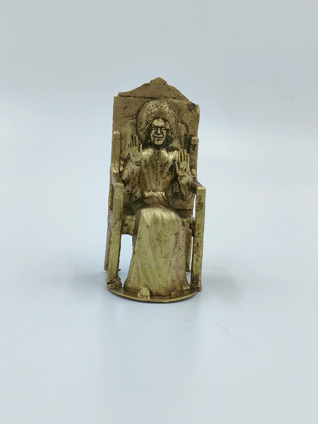 Small brass sculpture of Sai Baba sitting on a chair with hands raised