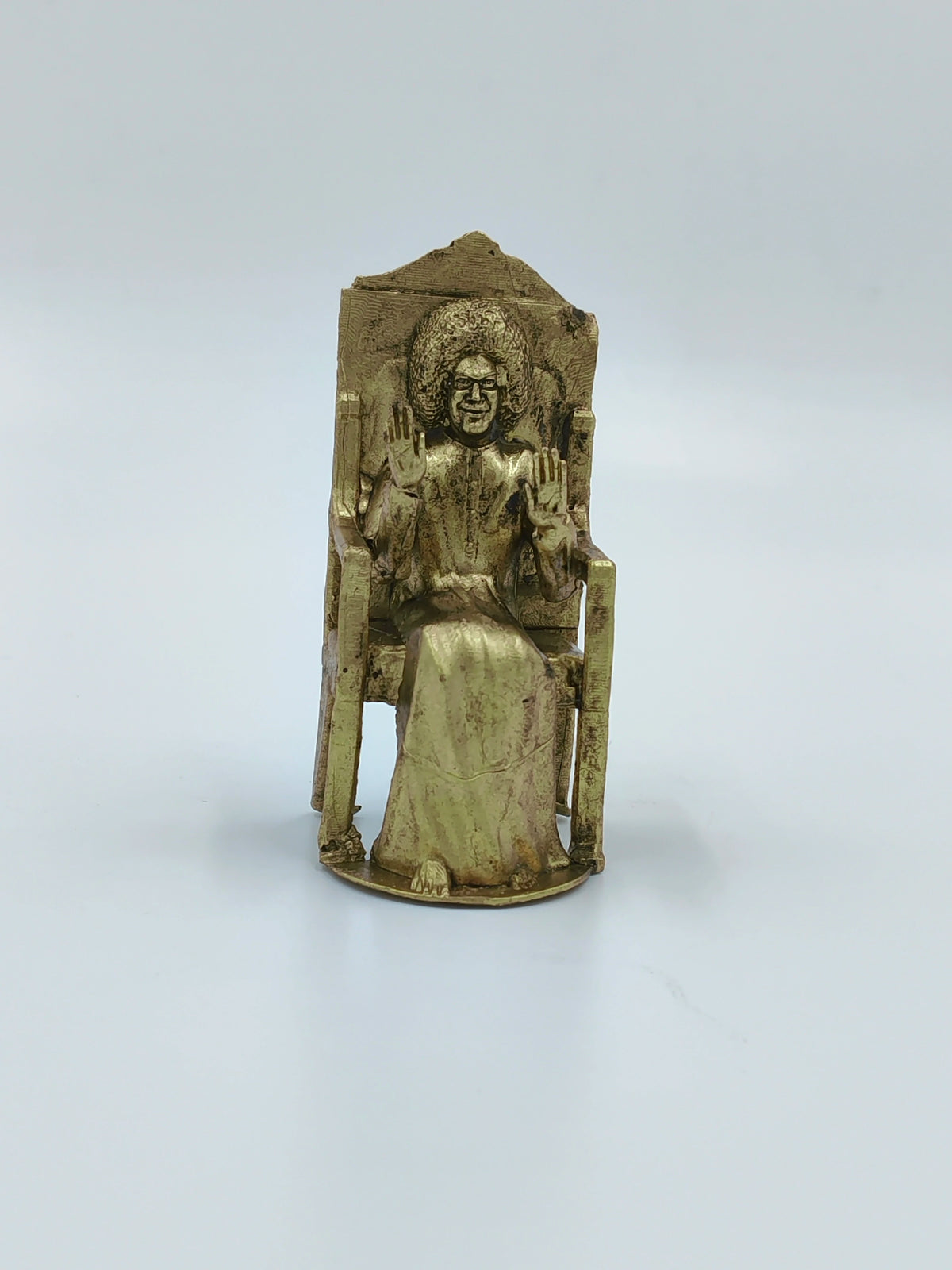 Small brass sculpture of Sai Baba sitting on a chair with hands raised