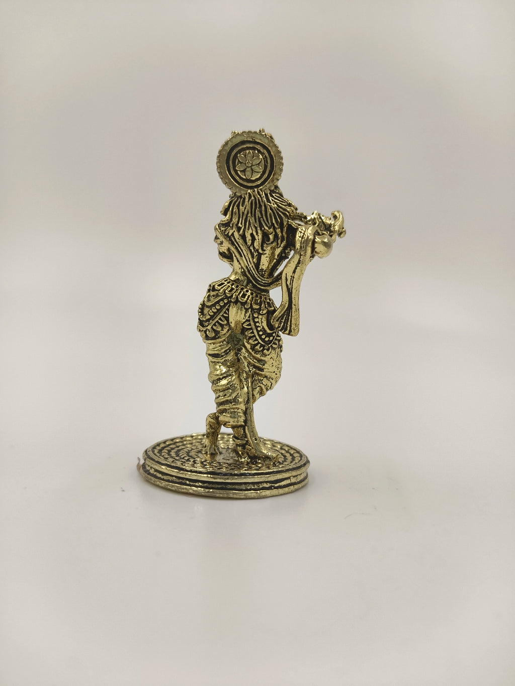Back view of a mini brass Krishna statue standing on a round base
