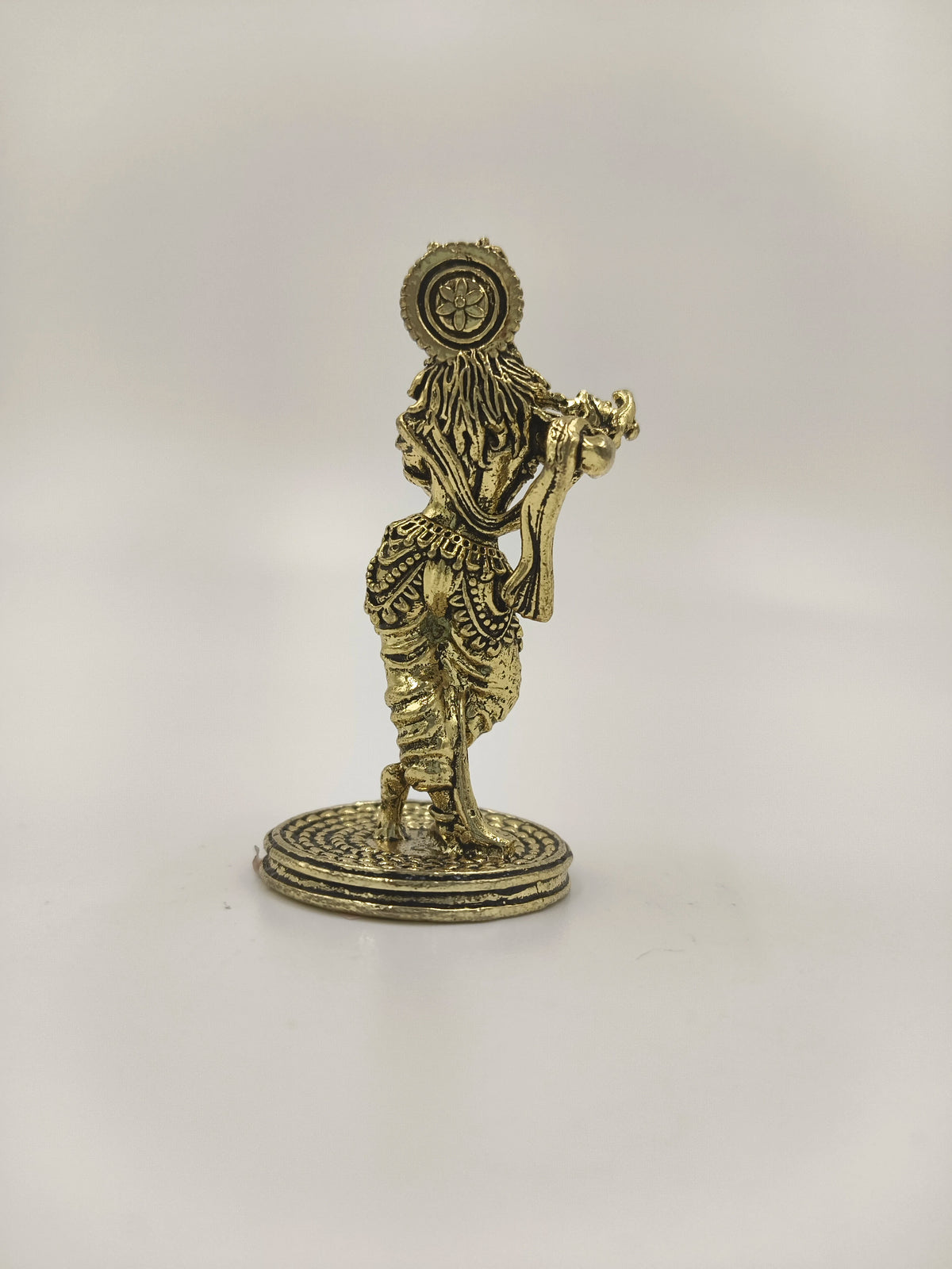 Back view of a mini brass Krishna statue standing on a round base