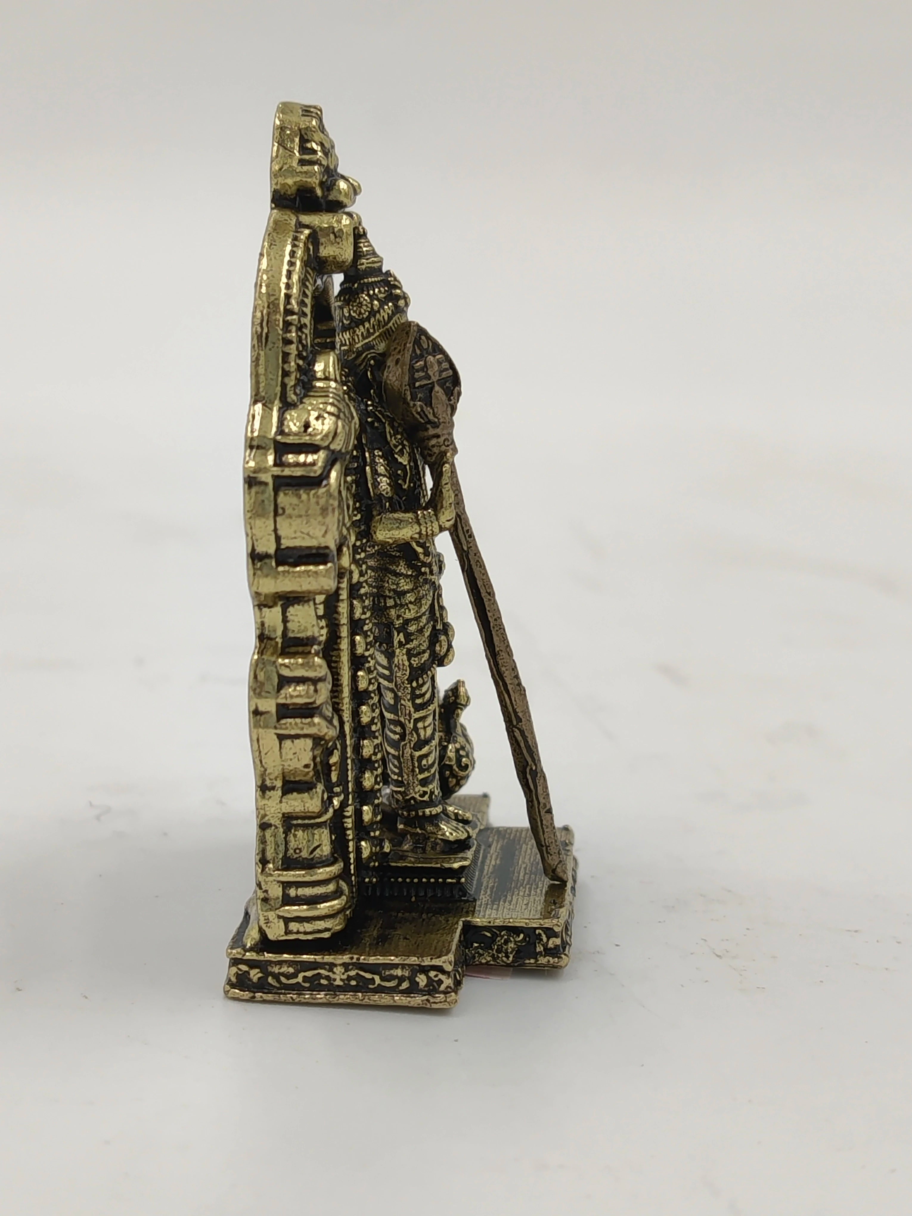 Side view of small brass Murugan statue holding spear with detailed base