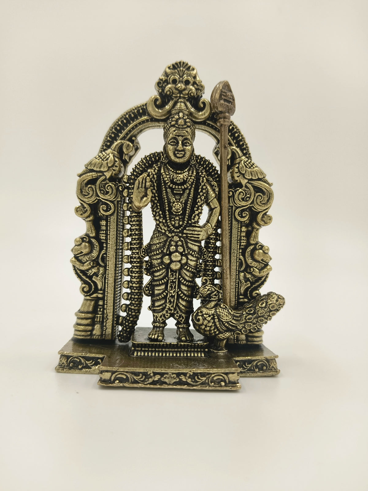 Small brass sculpture of deity Murgan with ornate arch and peacock