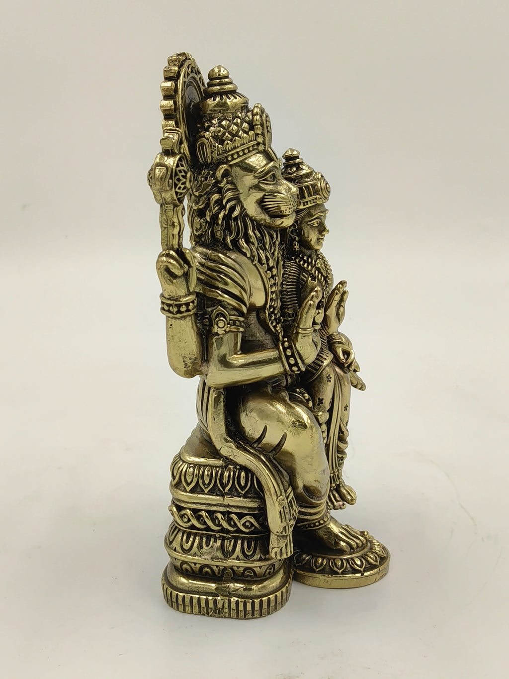 Side view of brass Narasimha sculpture seated on decorative pedestal