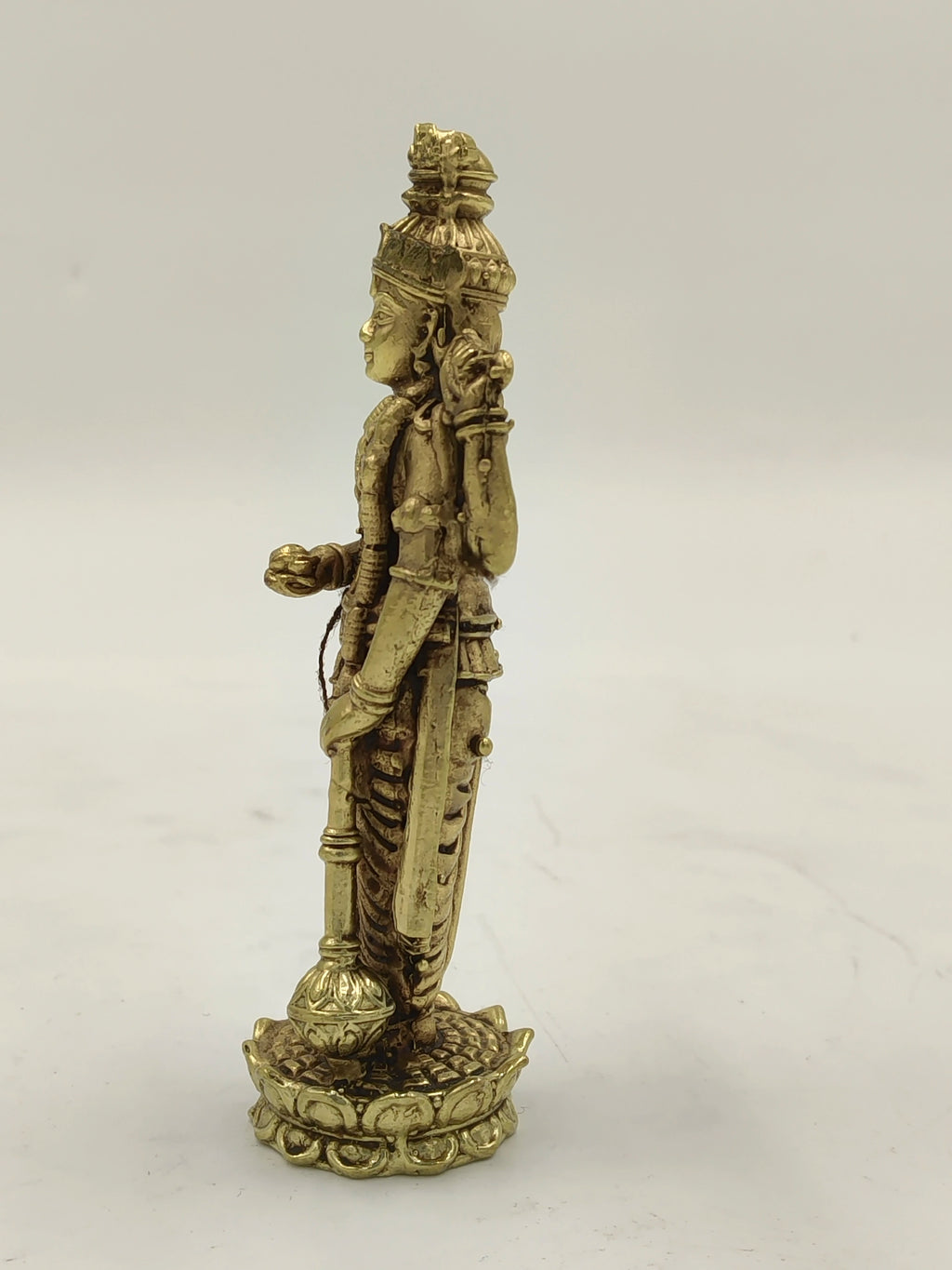 Side view of small brass Vishnu sculpture standing on decorative base