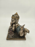 Polyresin sculpture of playful baby Ganesh reclining with a bowl of sweets