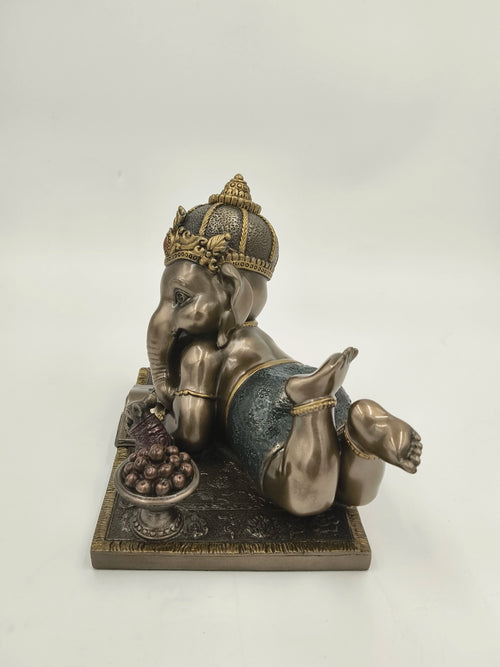 Polyresin sculpture of playful baby Ganesh reclining with a bowl of sweets