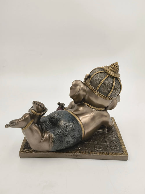 Rear view of a polyresin sculpture of playful baby Ganesh lying on a decorative base