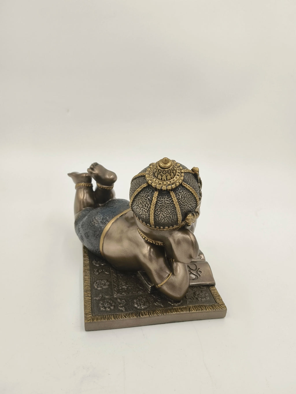 Polyresin sculpture of a baby Ganesh lying on stomach reading a book, rear view