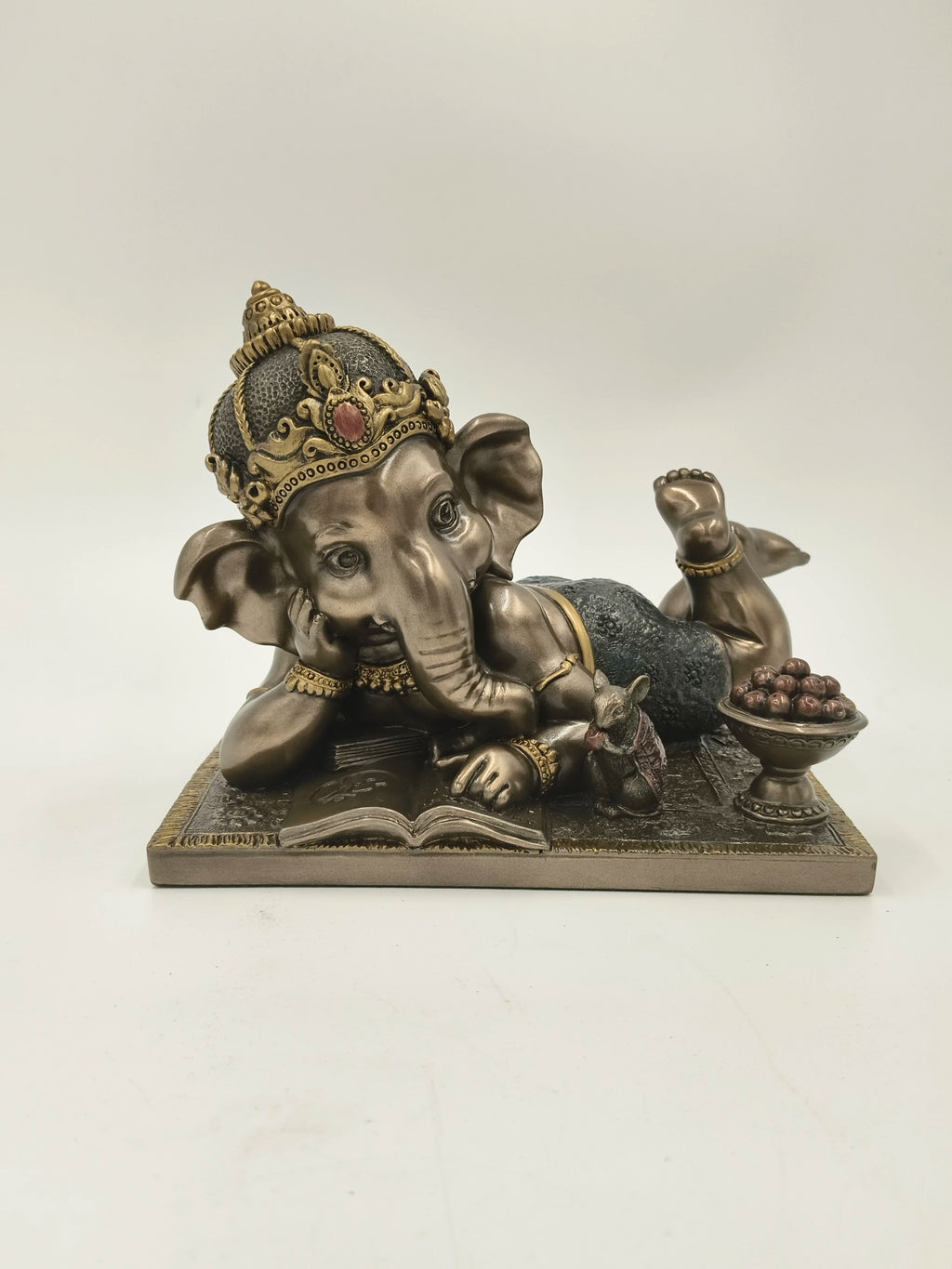Polyresin sculpture of playful baby Ganesh lying on side with book and mouse