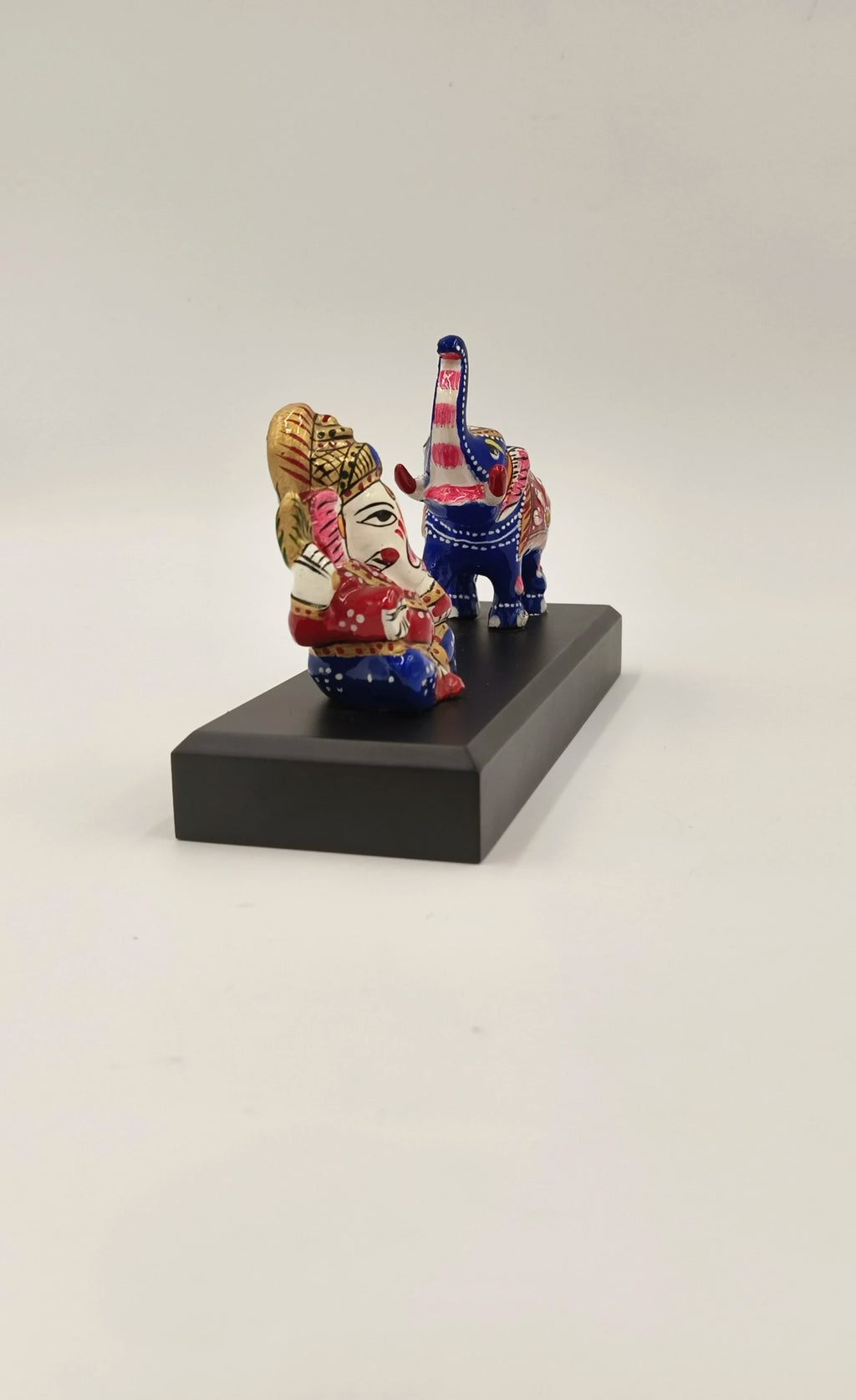 colorful brass Ganesh idol seated next to decorated elephant figurine on black base