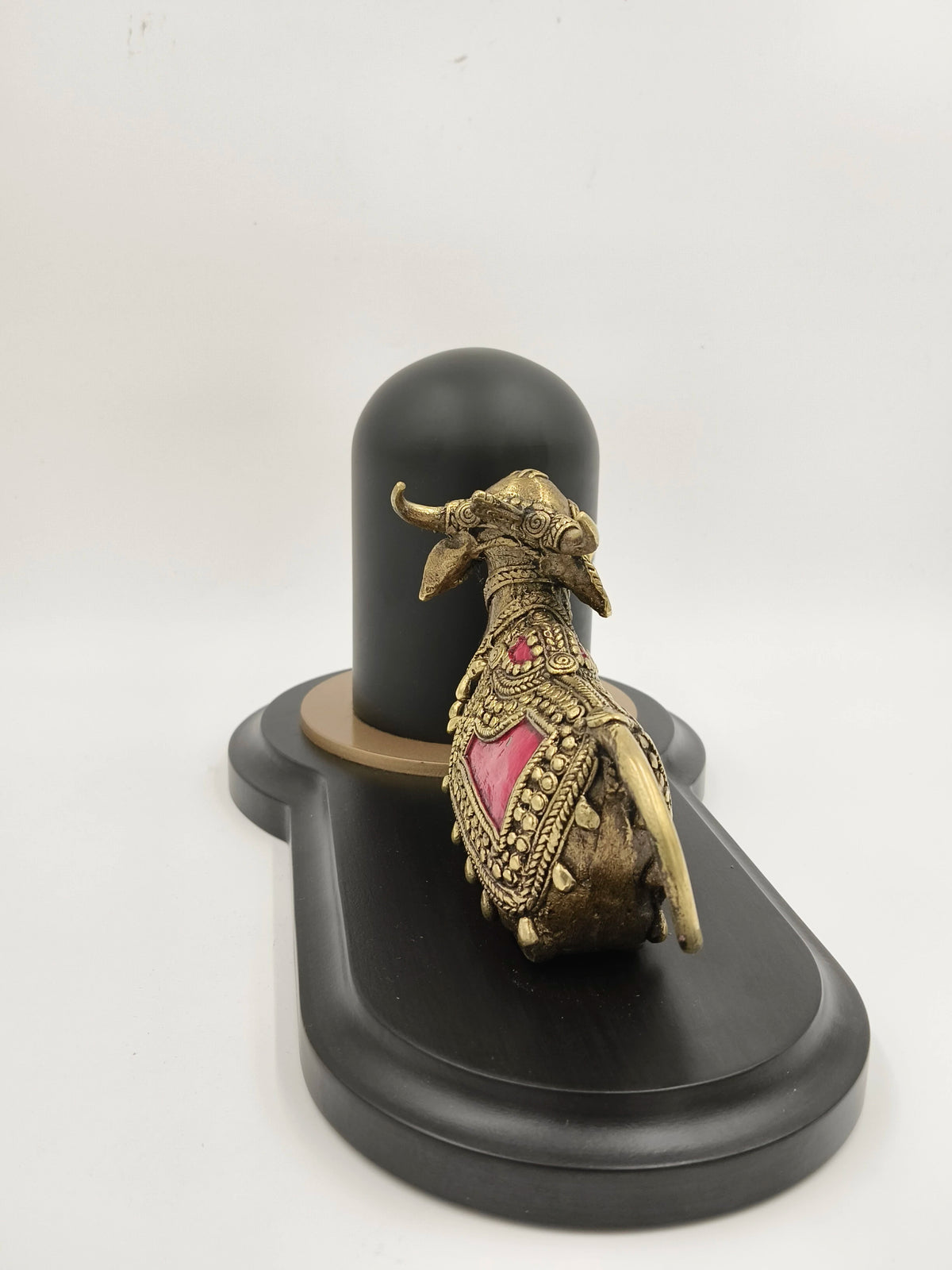 Brass Nandhi figurine with decorative details beside black Shivling on base