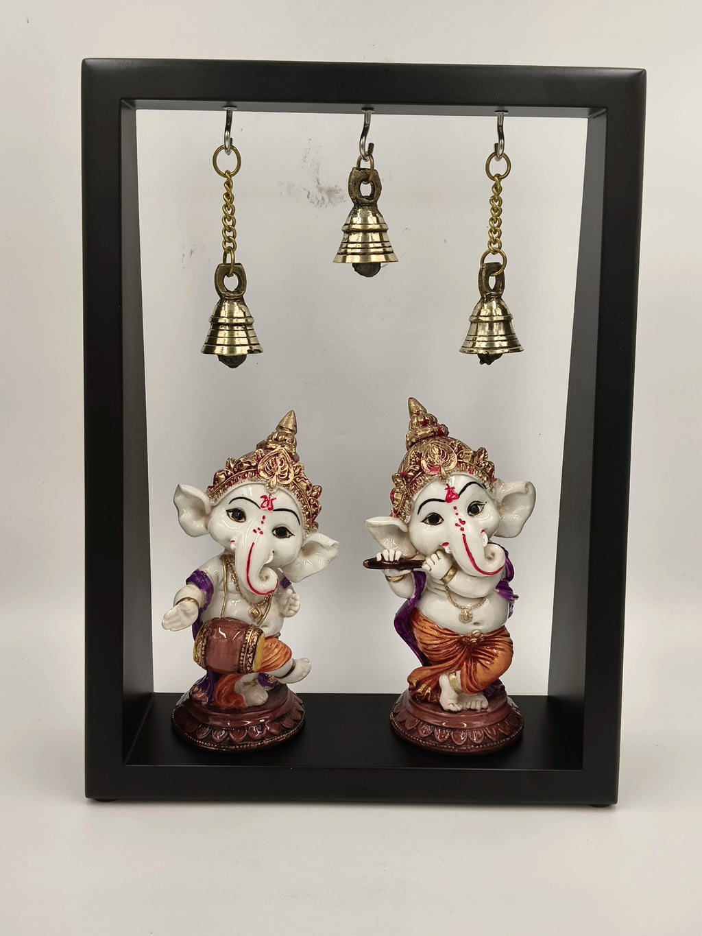 Black frame with two musical brass Ganesha idols and three hanging brass bells
