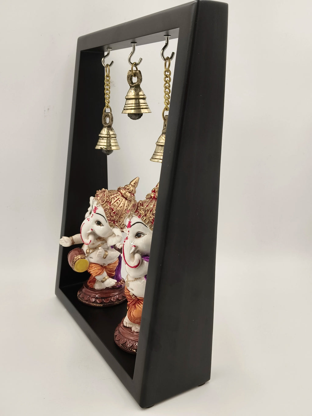 Large brass Ganesha figurines in a black frame with hanging brass bells side view