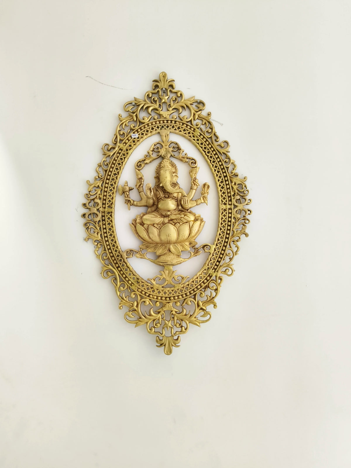 large brass wall hanging featuring Ganesh seated on lotus with ornate oval frame