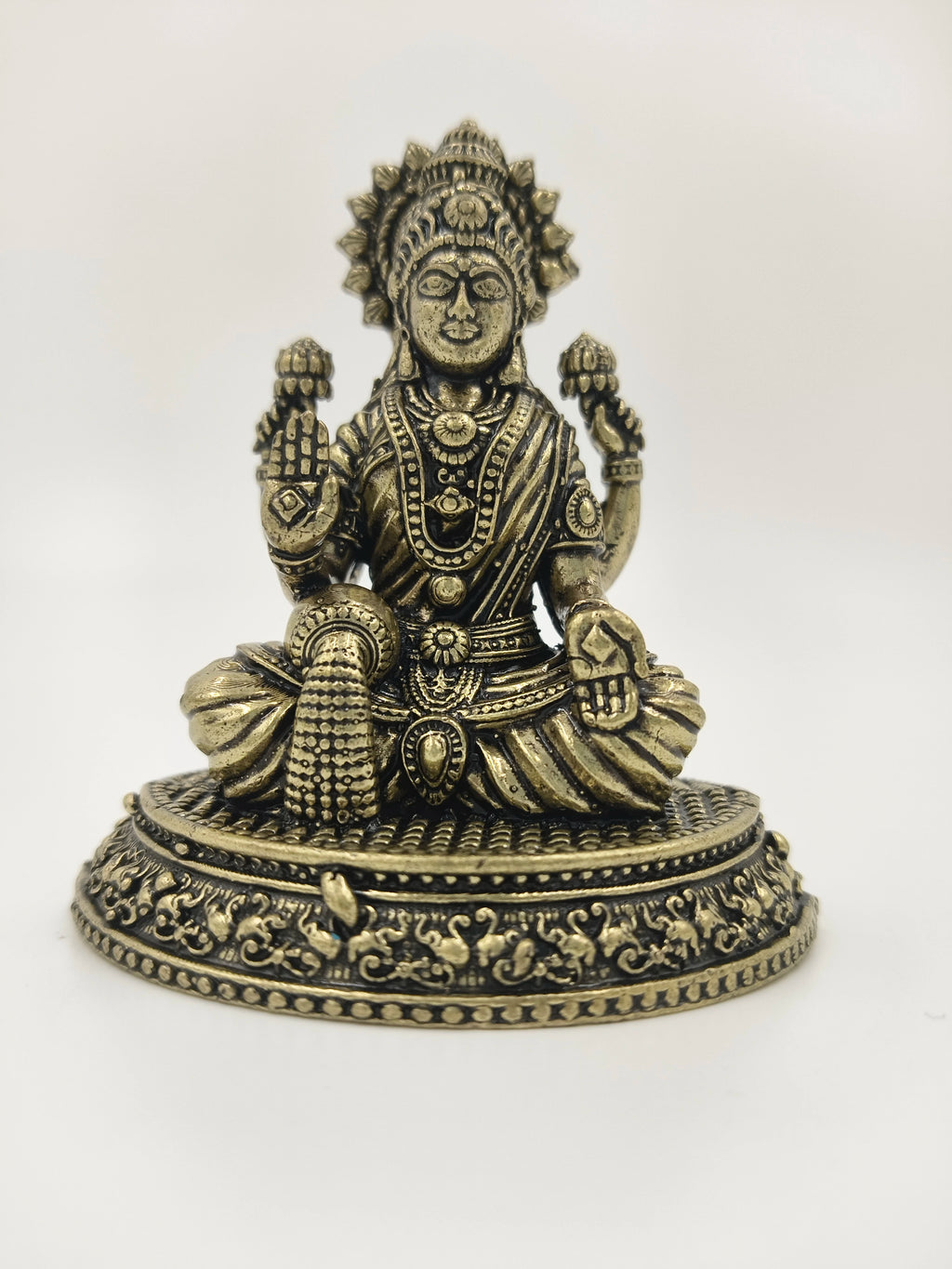 Small brass Lakshmi statue seated on ornate circular base with detailed carvings