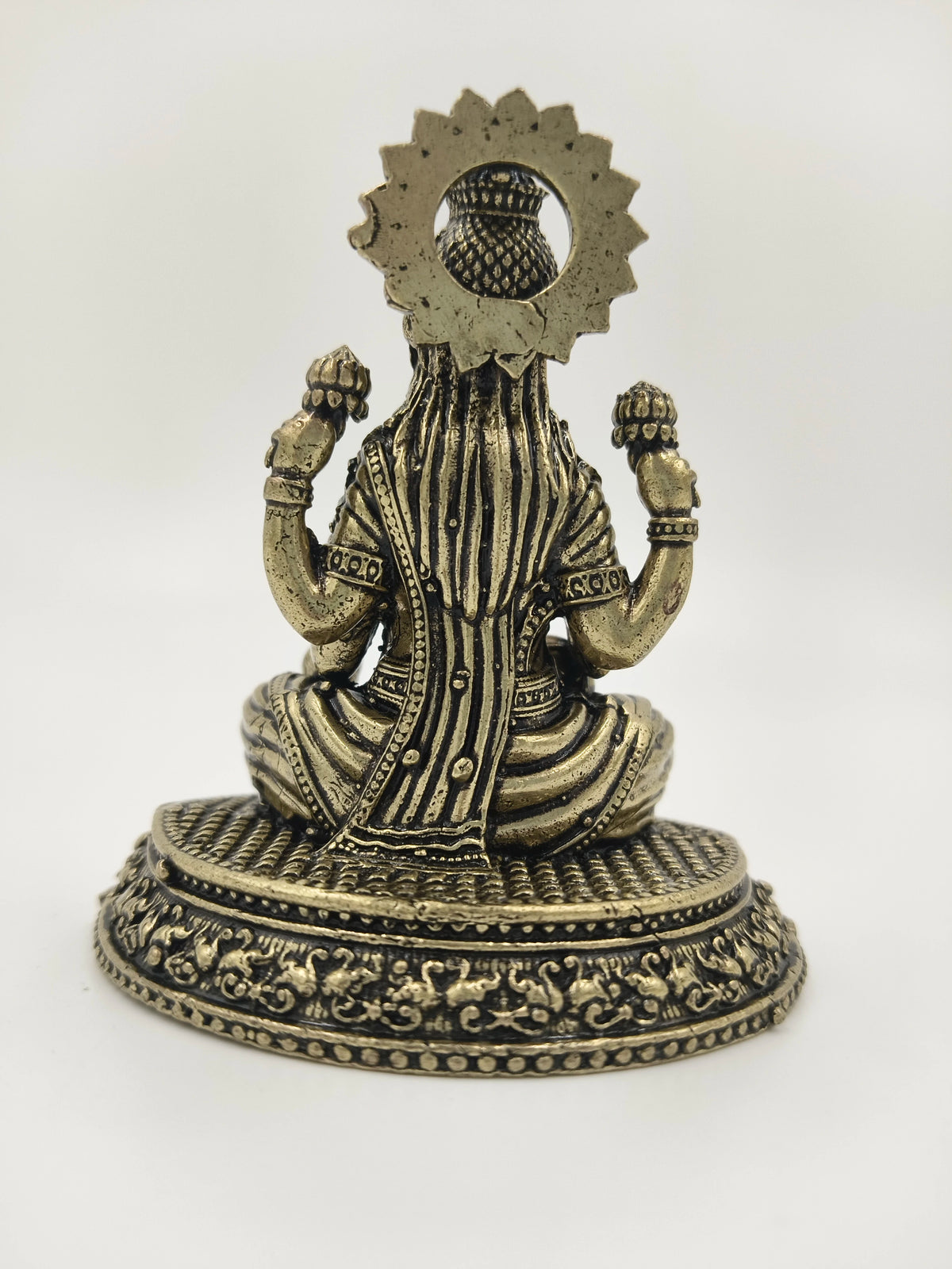 Back view of small brass Lakshmi statue seated on detailed base