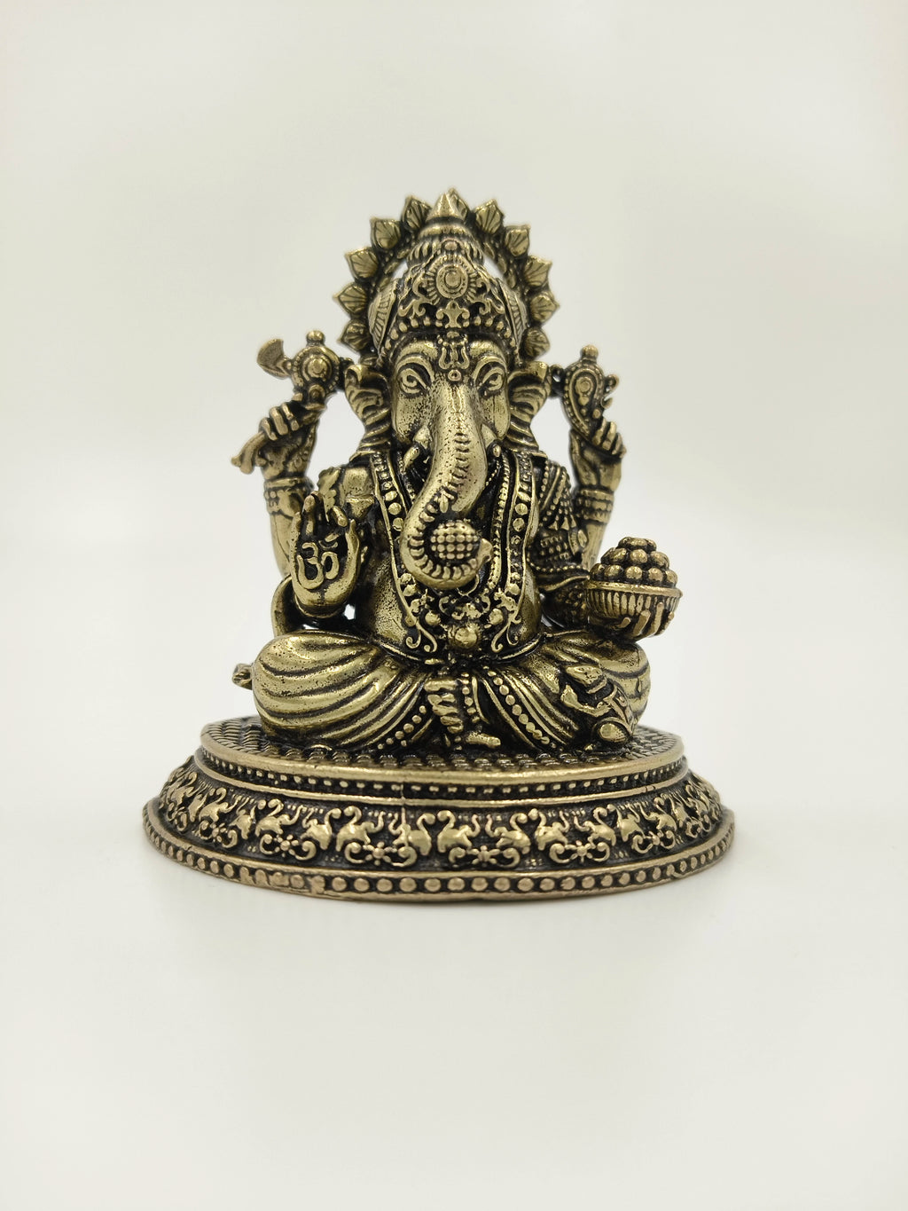 Small brass Ganesh sculpture seated with decorative base and detailed carvings