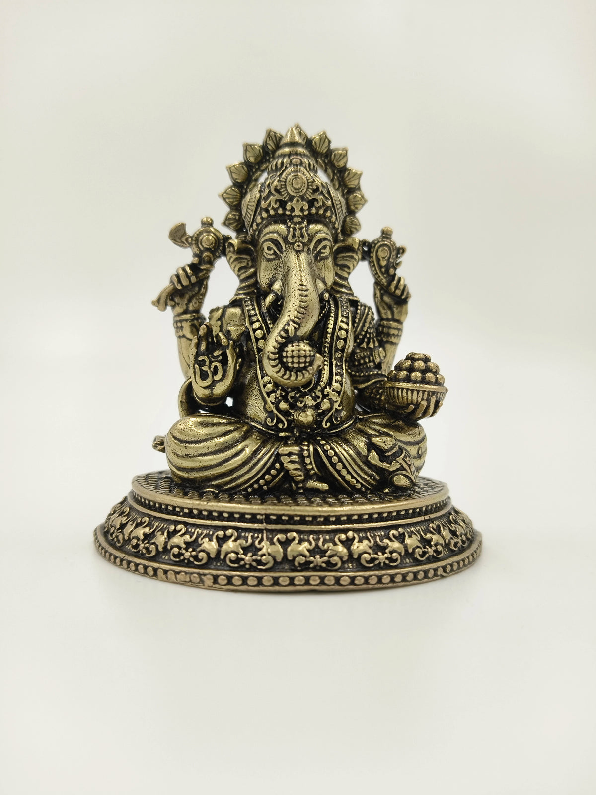 Small brass Ganesh sculpture seated with decorative base and detailed carvings