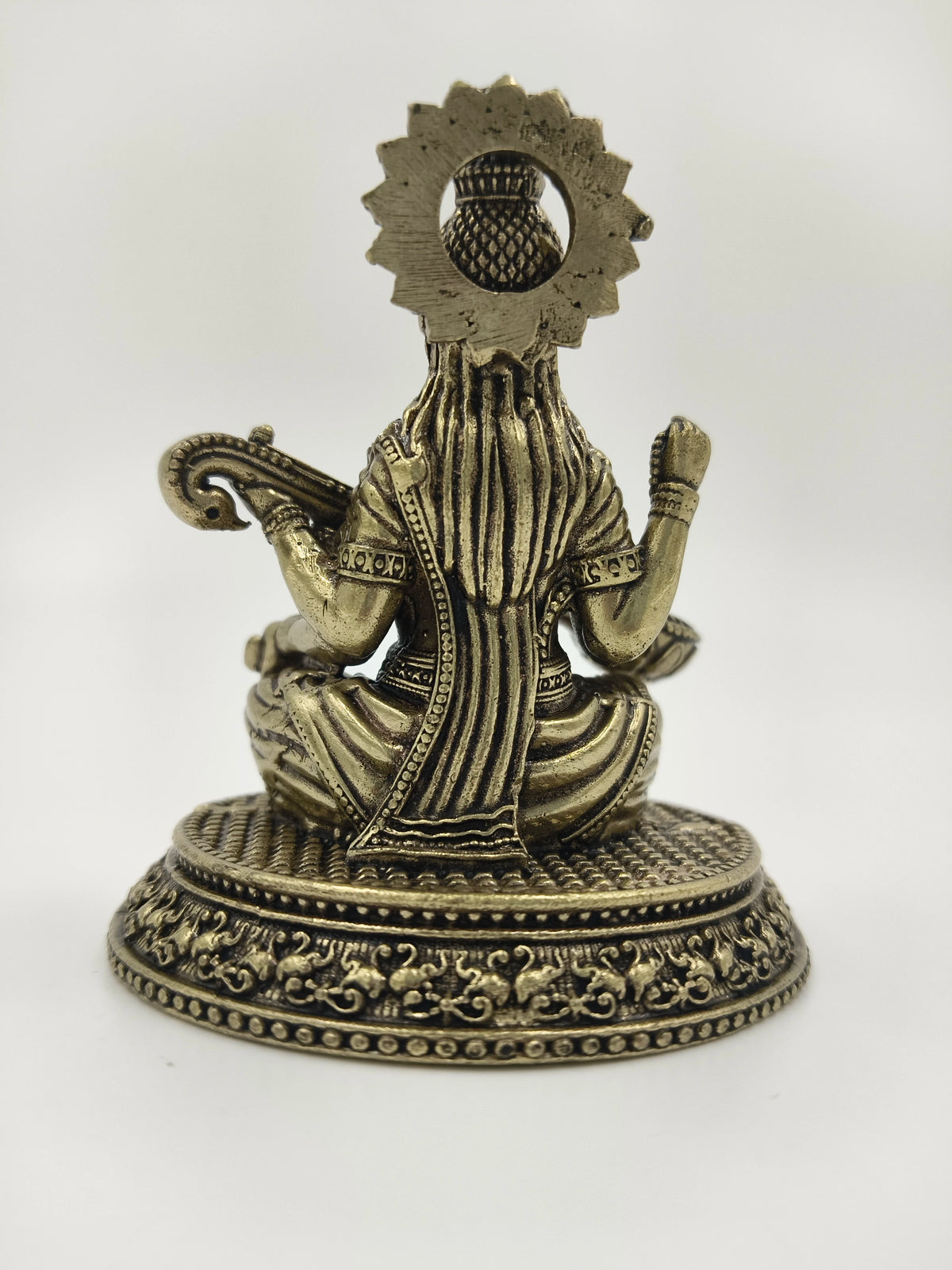 Small brass statue of Saraswathi shown from the back sitting on decorated base