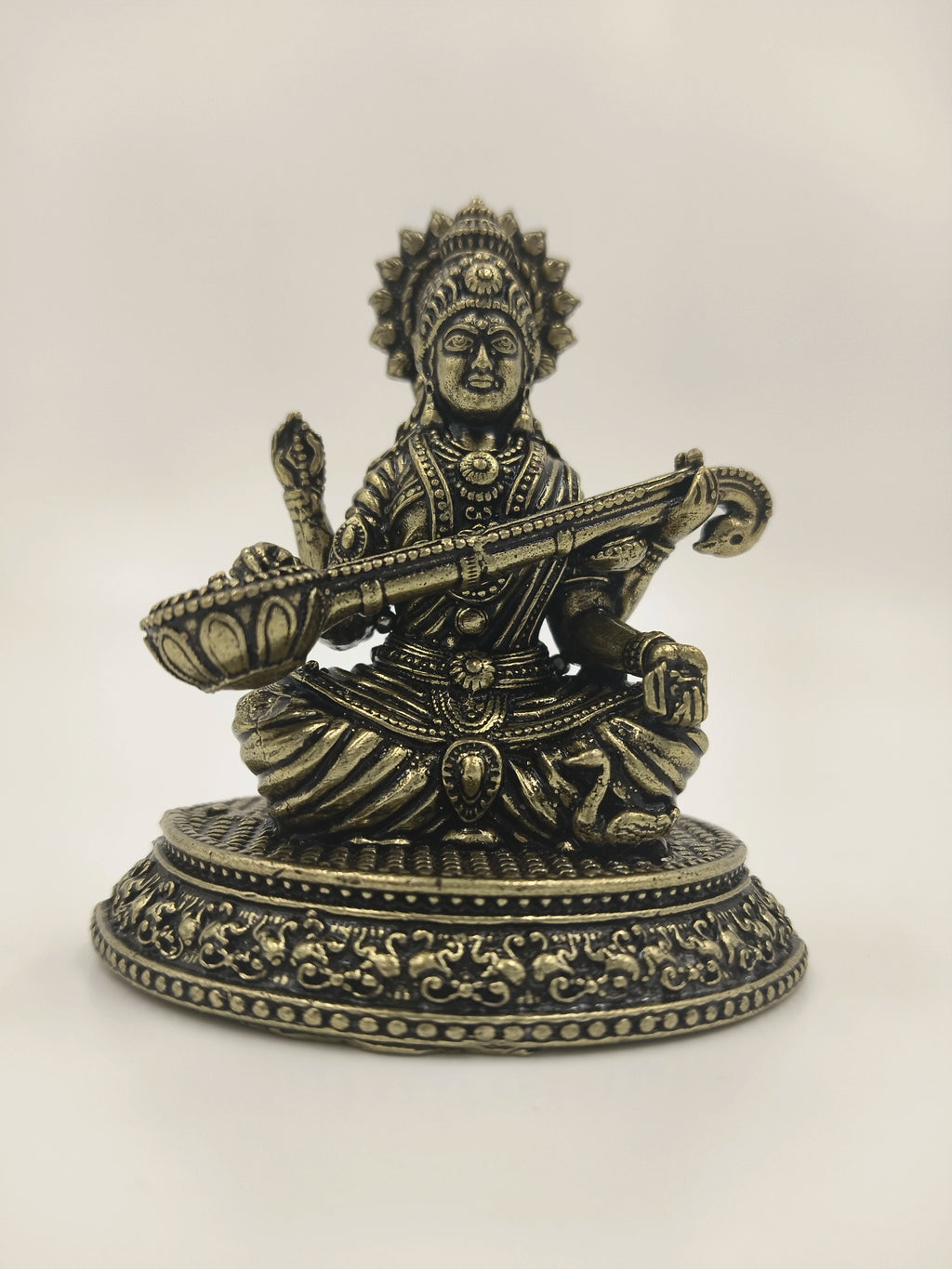 Small brass Saraswathi statue seated on decorated round base playing veena